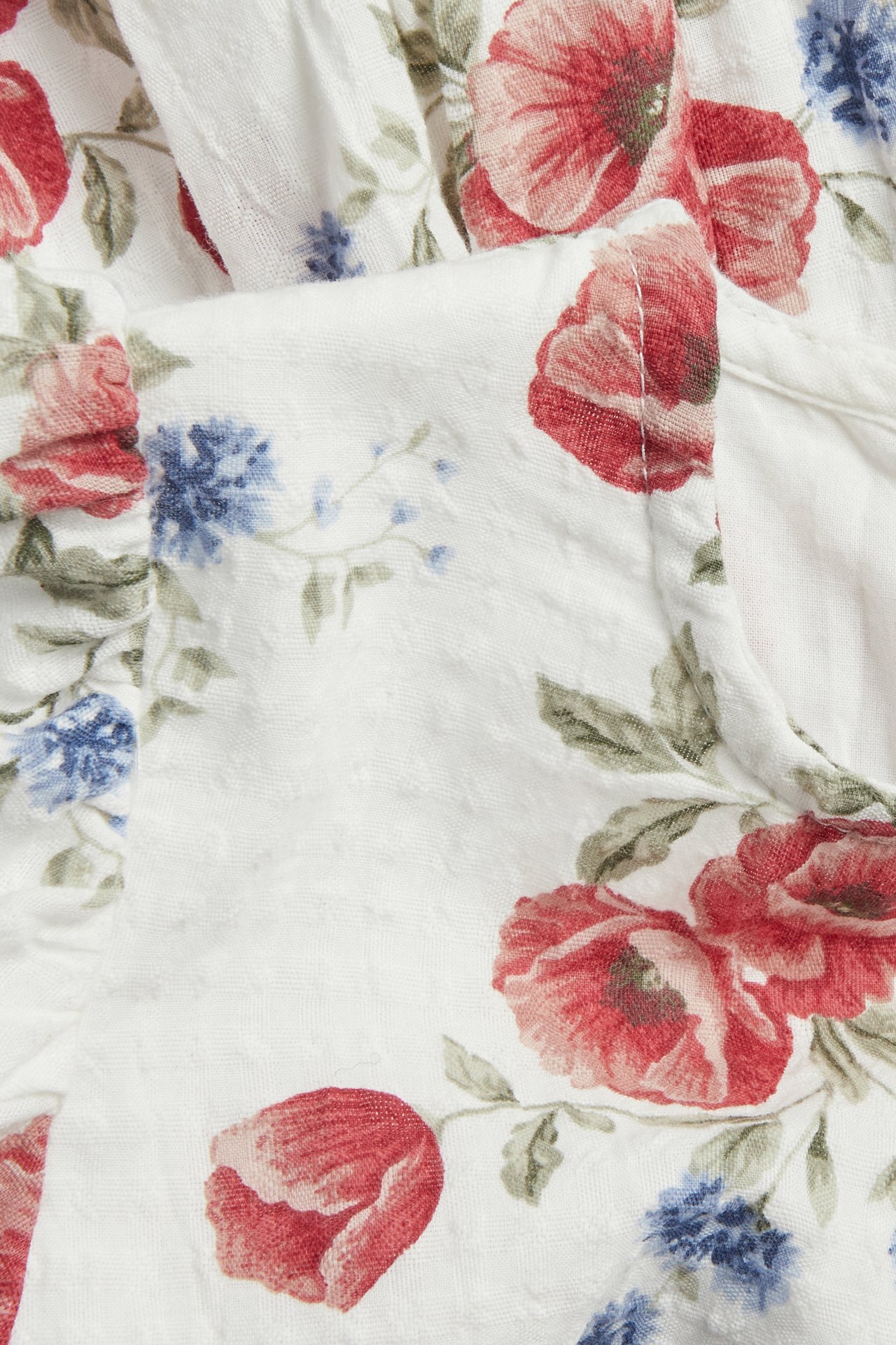 Close-up of off-white woven floral dress fabric with red and blue flowers and green leaves.