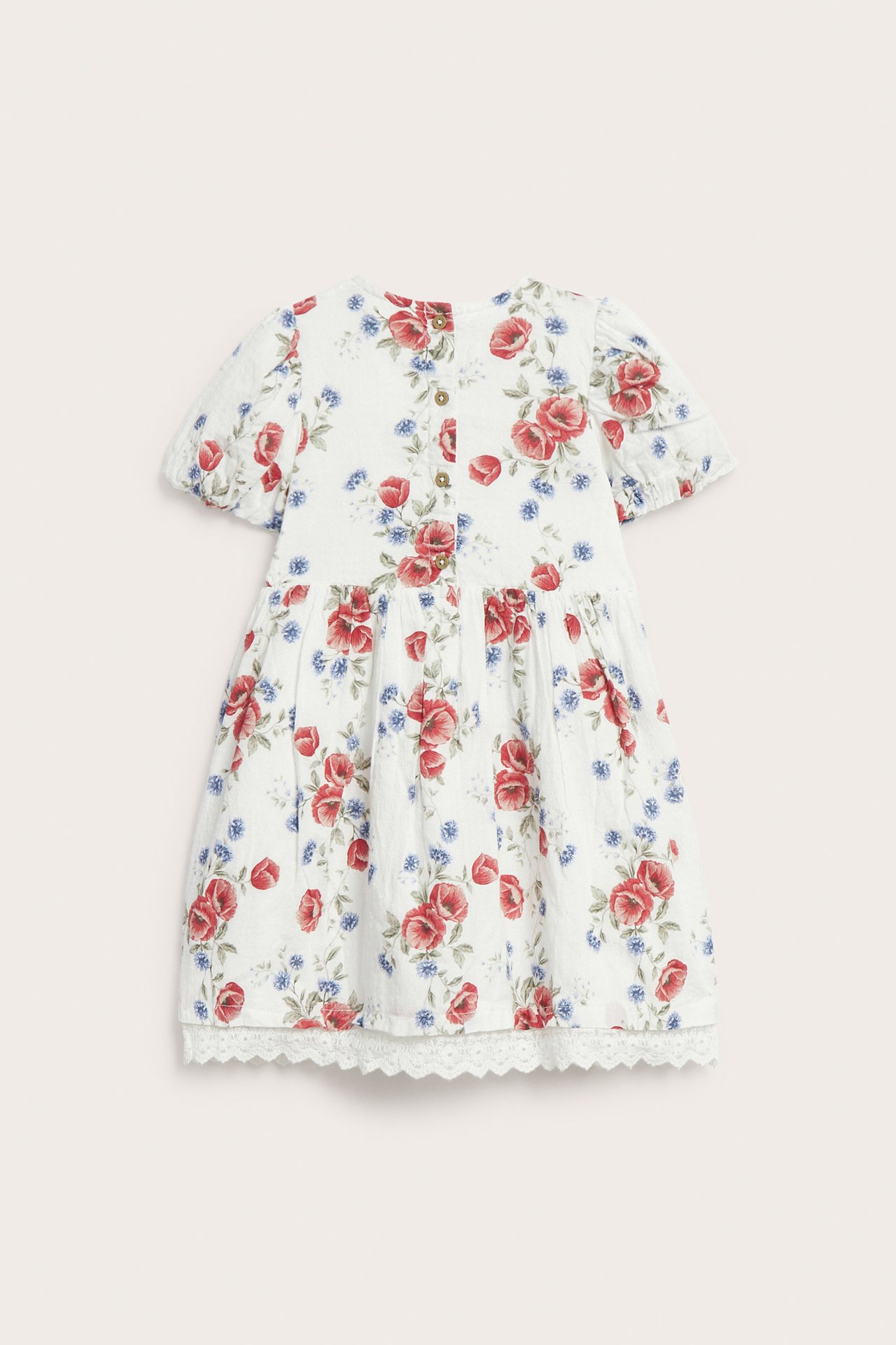 Back view: Kid's off-white floral dress with red/blue flowers, balloon sleeves, back buttons, and lace hem.