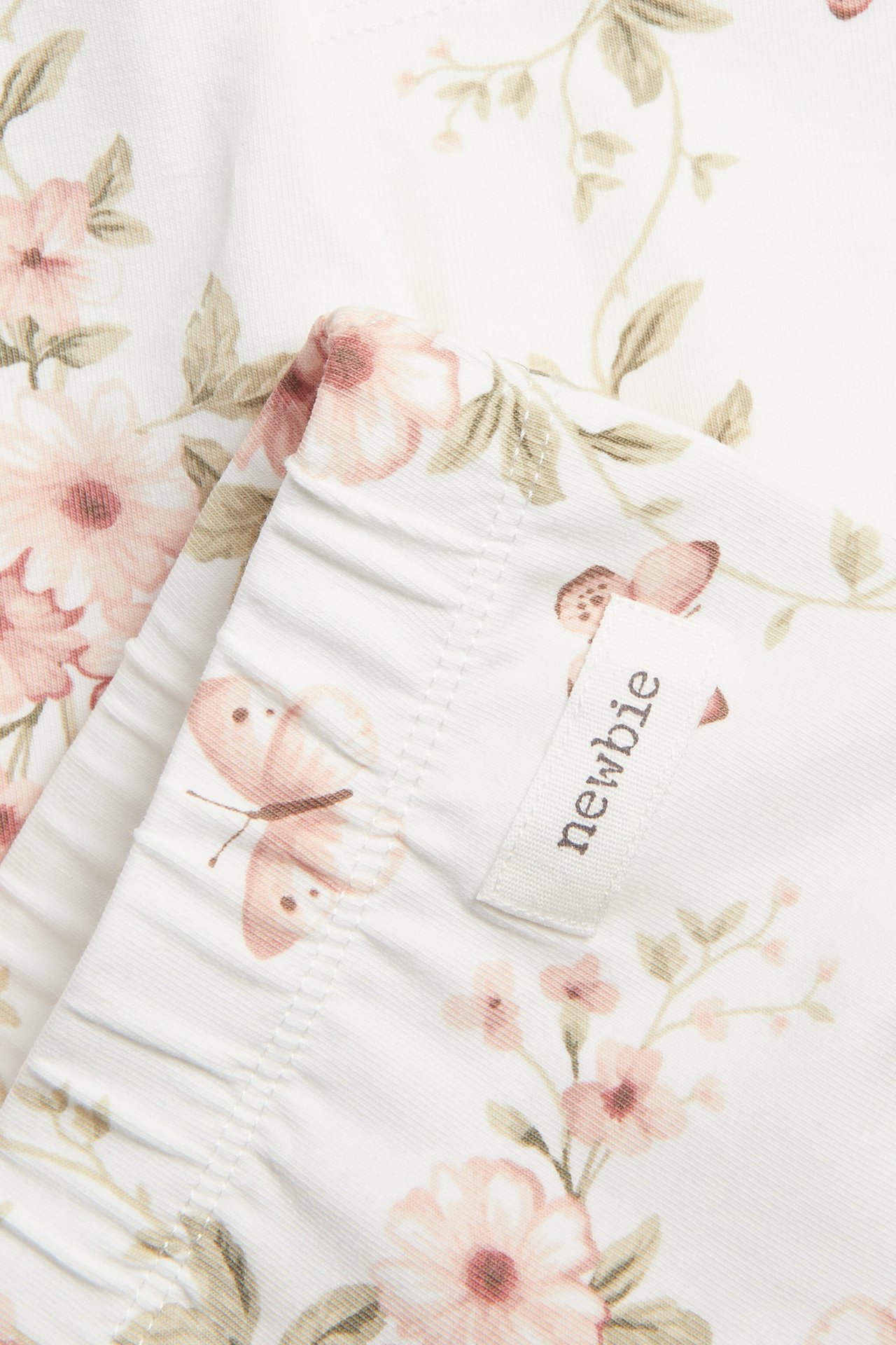 Close-up of offwhite tricot cycling shorts with a pink floral and butterfly print, showing a Newbie tag.