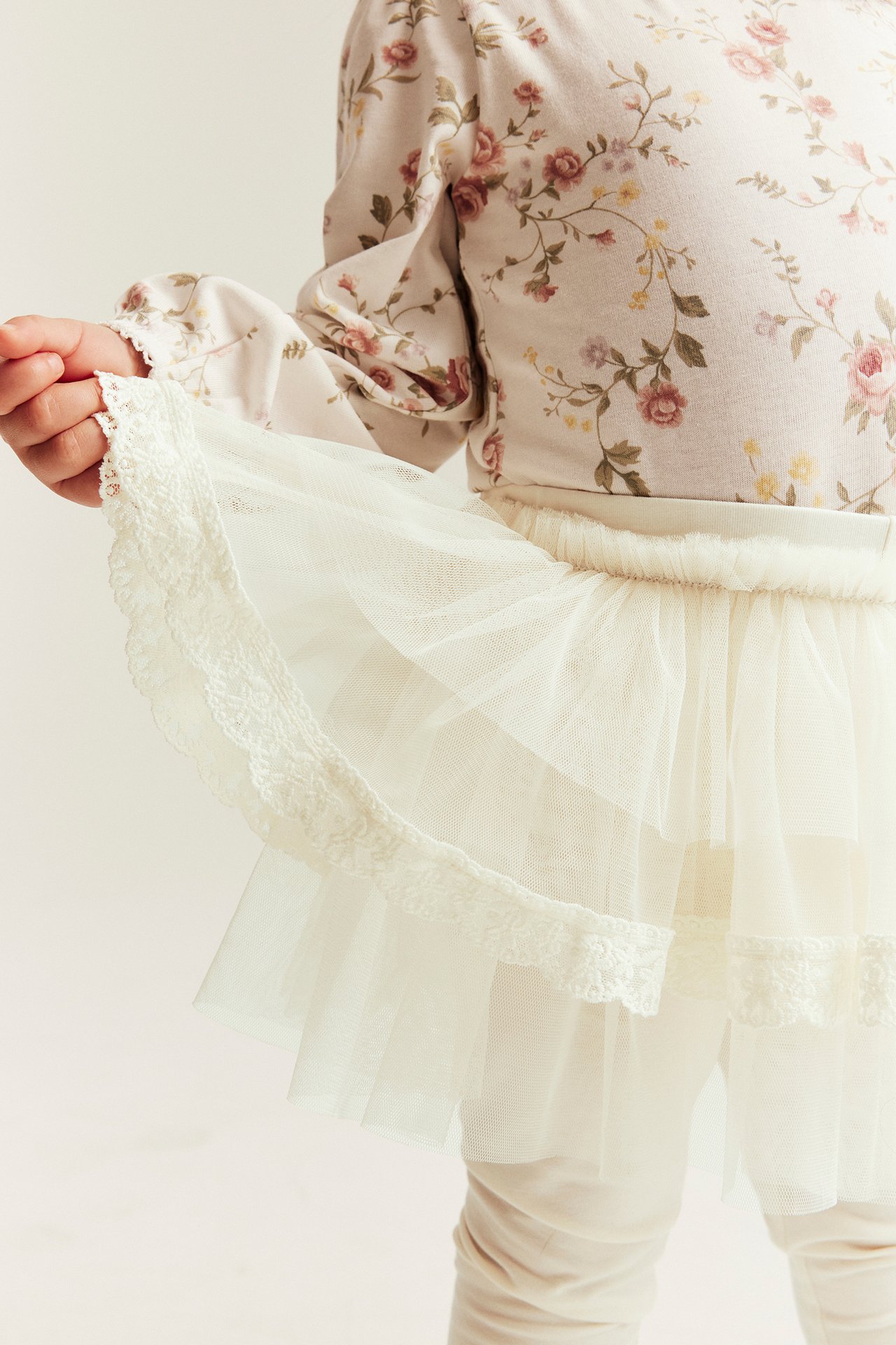 Front view of kid in offwhite leggings with tiered, lace-trimmed tulle skirt and floral top.