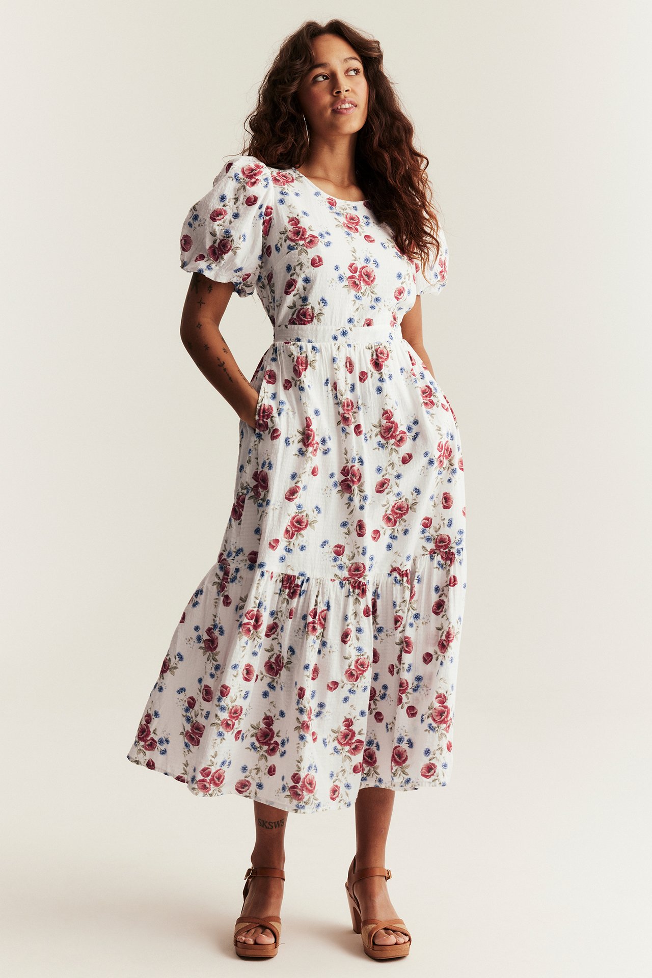 Front view of a woman wearing an off-white floral midi dress with balloon sleeves and brown platform sandals.
