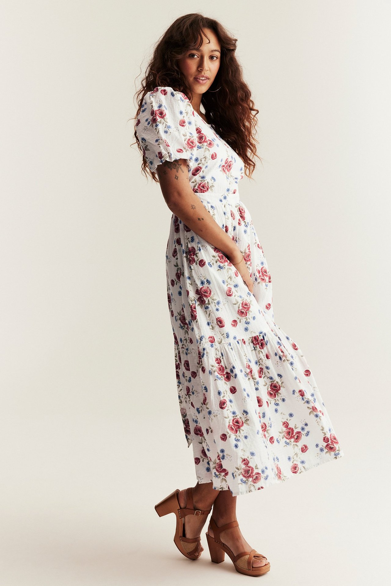 Woman in off-white dress with red, blue floral pattern, balloon sleeves, and brown platform sandals.