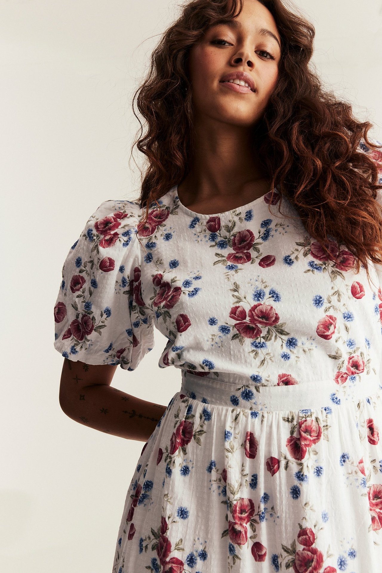 Front view: Woman in off-white floral dress with red and blue flowers, featuring balloon sleeves.