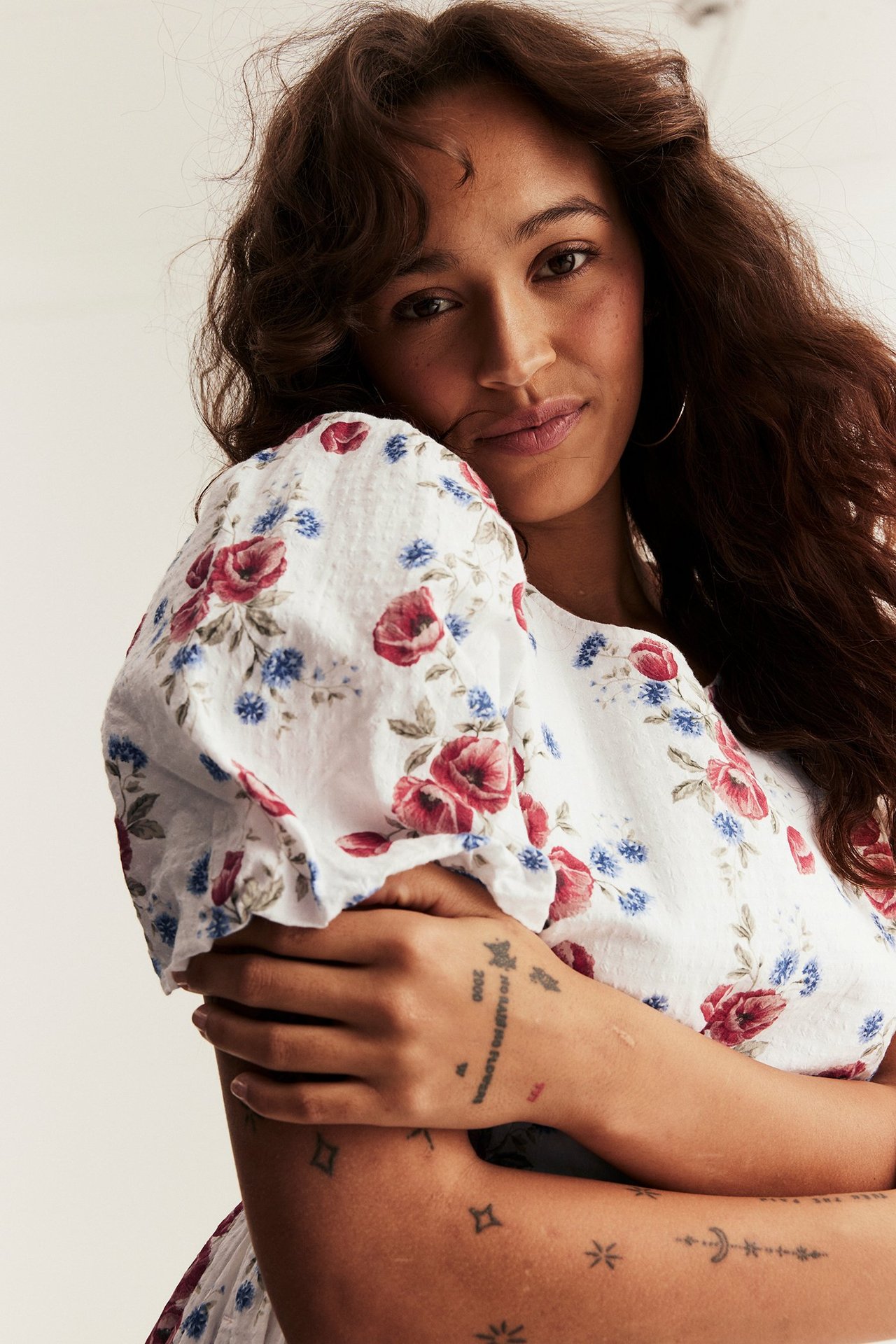 Close-up of a woman wearing an off-white woven floral dress with red and blue flowers and balloon sleeves.