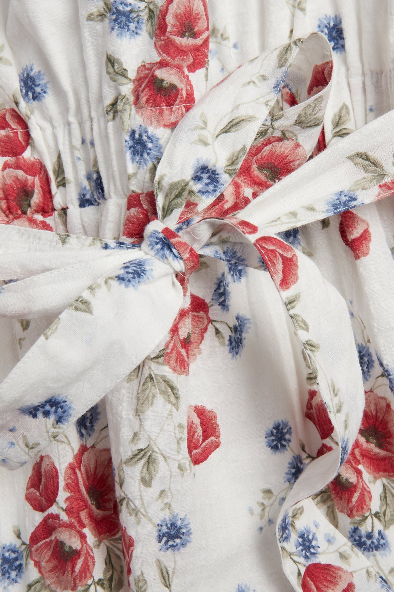 Nahaufnahme eines cremeweißen Blumenkleides mit roten Mohnblumen und blauen Blüten, mit einer Schleife.