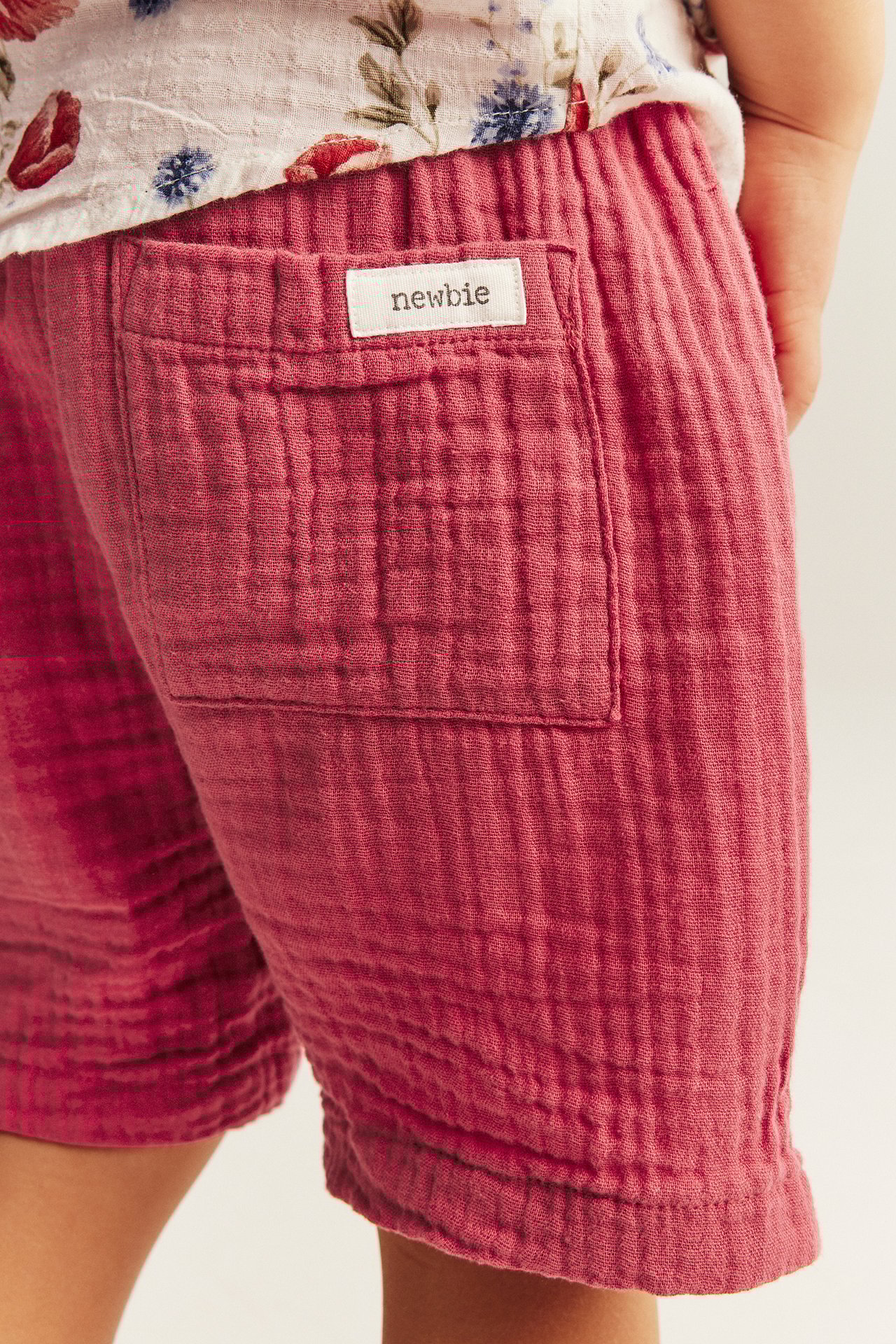 Nahaufnahme von texturierten roten gewebten Baumwollshorts für Kinder mit Gesäßtasche und Newbie-Etikett.