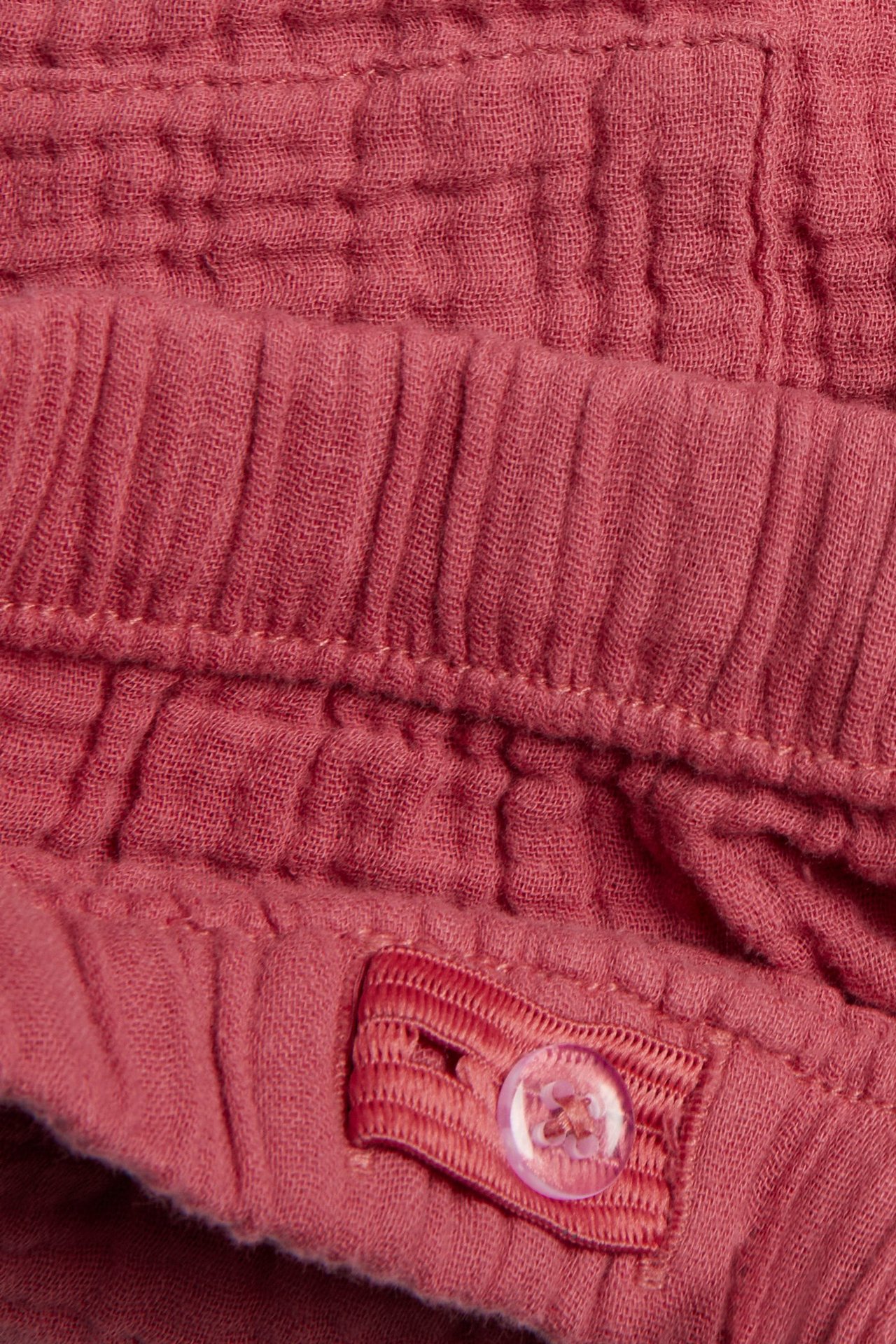 Nahaufnahme roter gewebter Baumwollshorts mit elastischem Bund und verstellbarem Knopfverschluss.