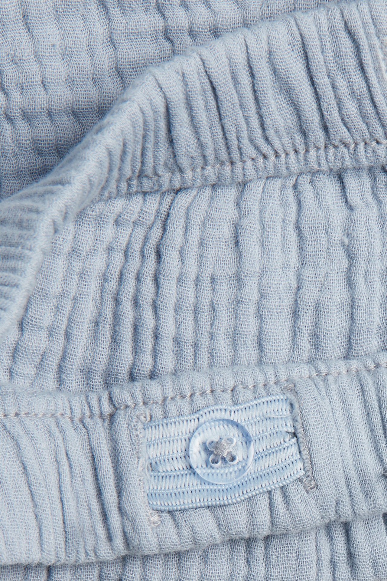 Nahaufnahme von hellblauen gewebten Baumwollshorts mit elastischem Bund und verstellbarem blauem Knopf.