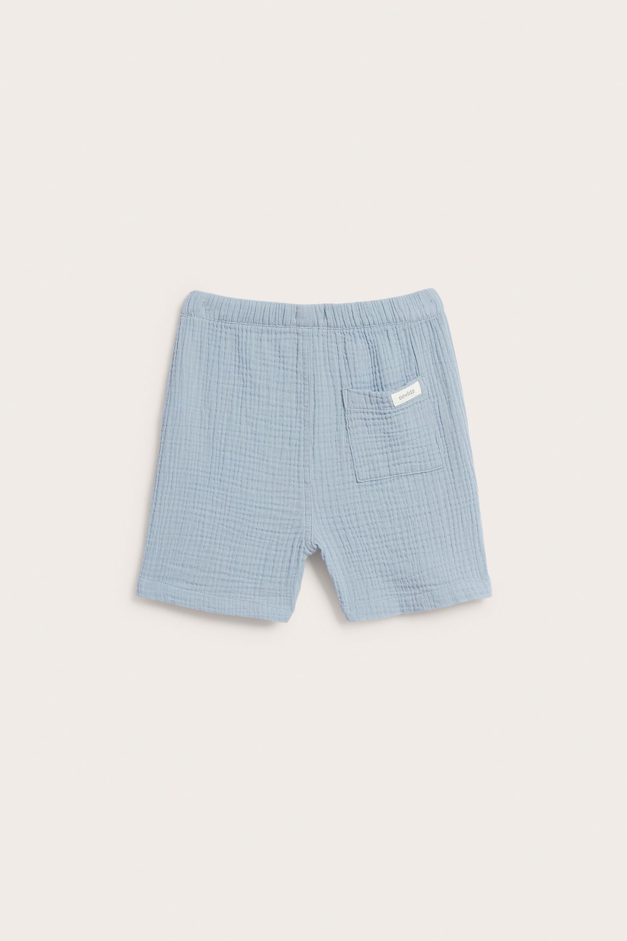Schräge Rückansicht hellblauer, gewebter Kindershorts mit Gummizugbund und einer aufgesetzten Gesäßtasche.