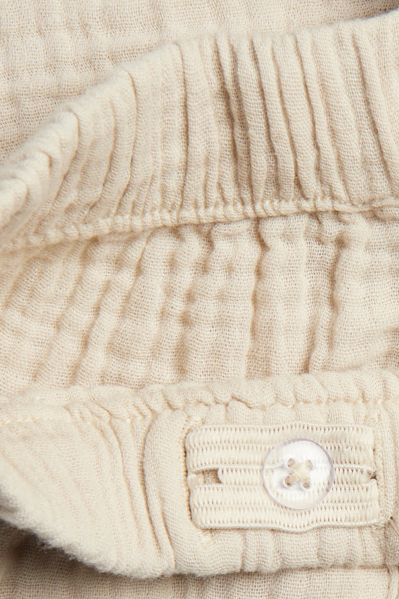 Close-up of off-white woven cotton shorts, showing the elastic waistband with an adjustable button tab.