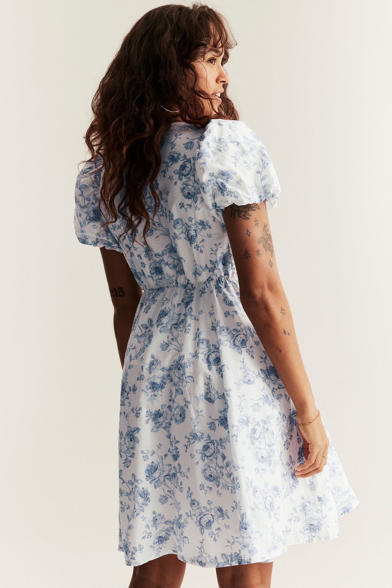 Side view of woman in off-white blue floral cotton dress with short puffy sleeves and flared skirt.