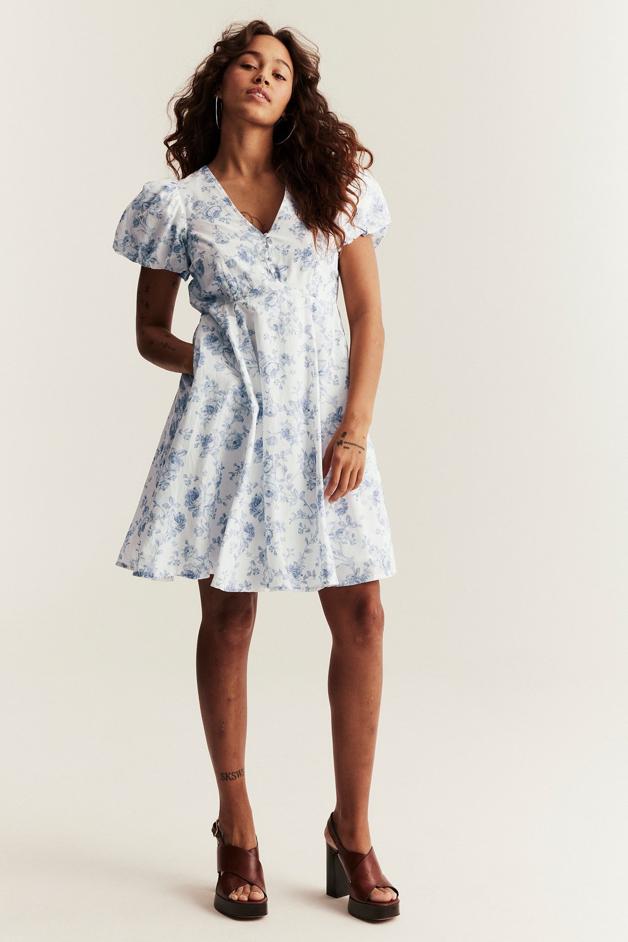 Woman in offwhite floral cotton dress with puff sleeves, brown platform sandals, and hoop earrings.