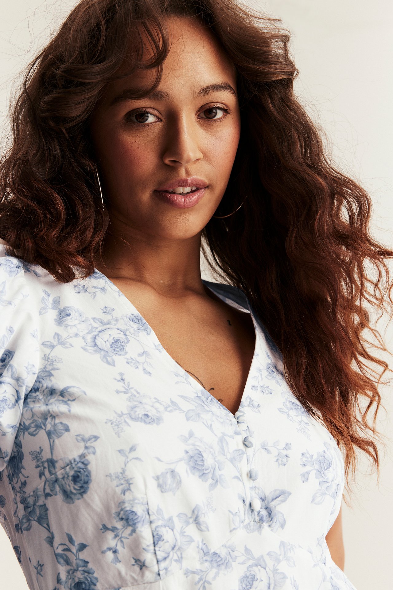 Nahaufnahme von vorne einer Frau in einem cremefarbenen Blumenkleid mit blauem Muster, Knöpfen und Puffärmeln.