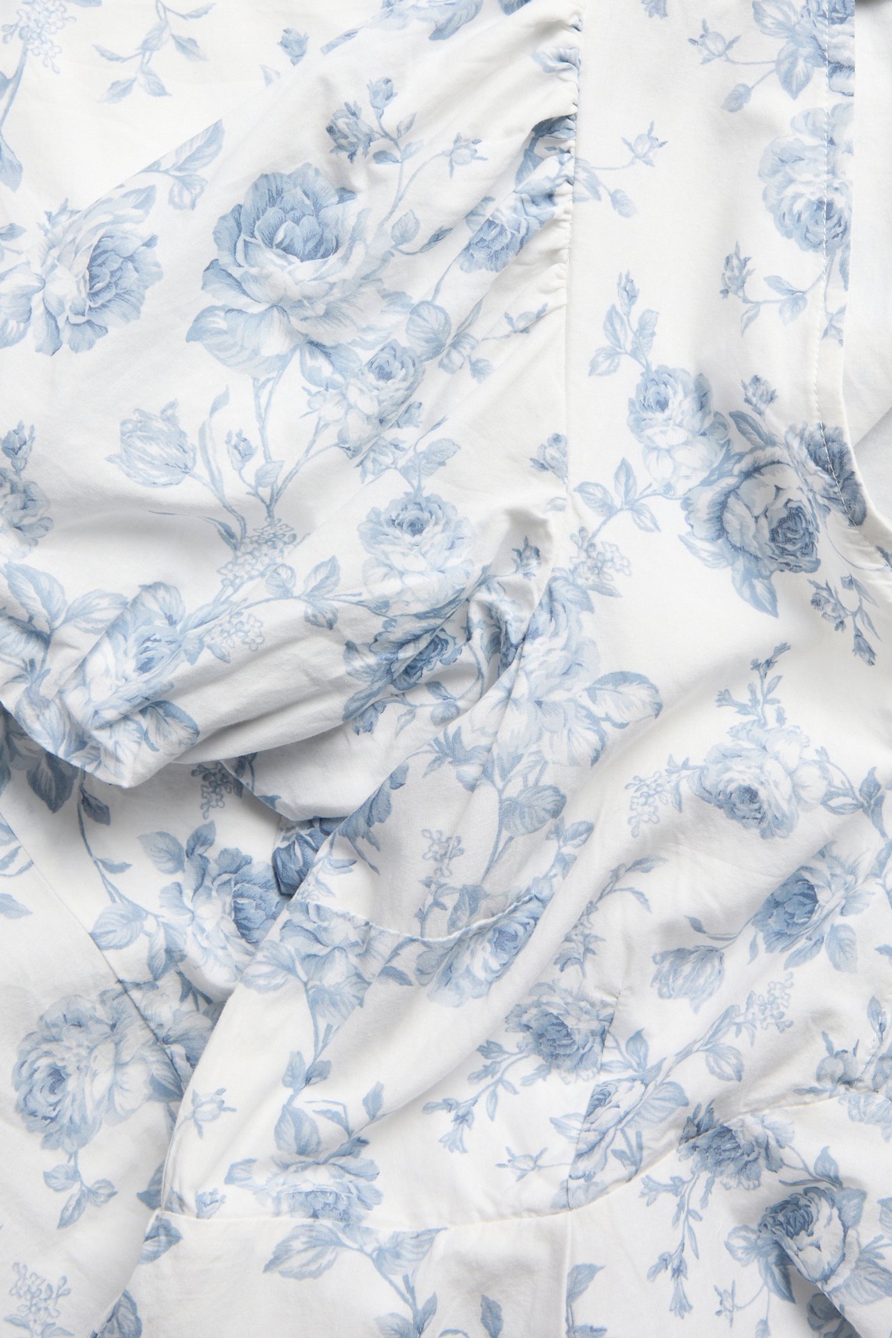 Nahaufnahme eines off-white Damen-Baumwollkleides mit hellblauem Blumenmuster, das ein Puffärmel-Detail zeigt.