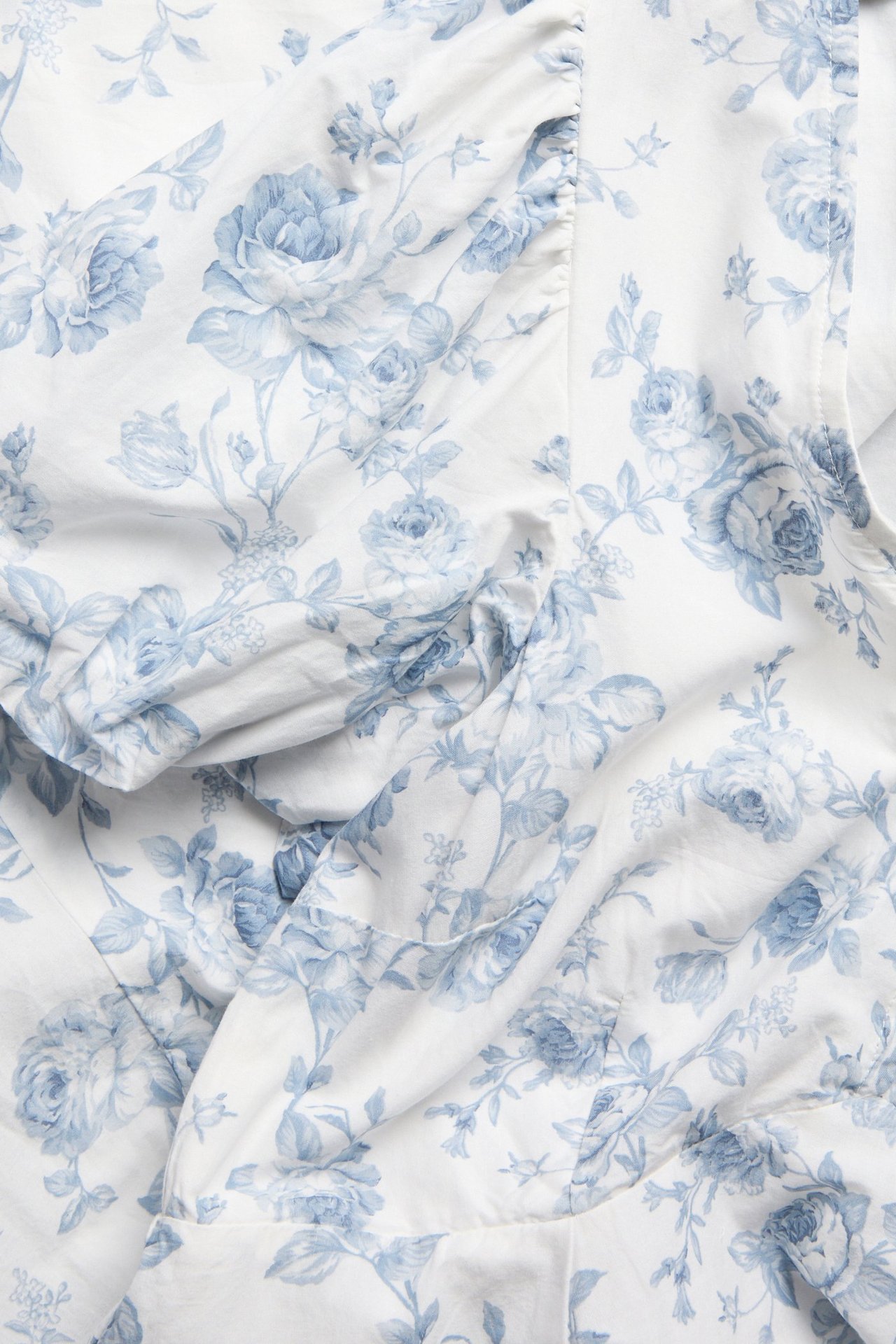 Nahaufnahme eines off-white Damen-Baumwollkleides mit hellblauem Blumenmuster, das ein Puffärmel-Detail zeigt.
