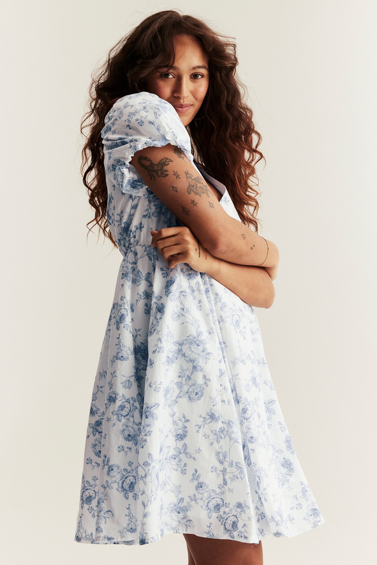 Side view of a woman in an off-white short cotton dress with a blue floral pattern and puffy sleeves.