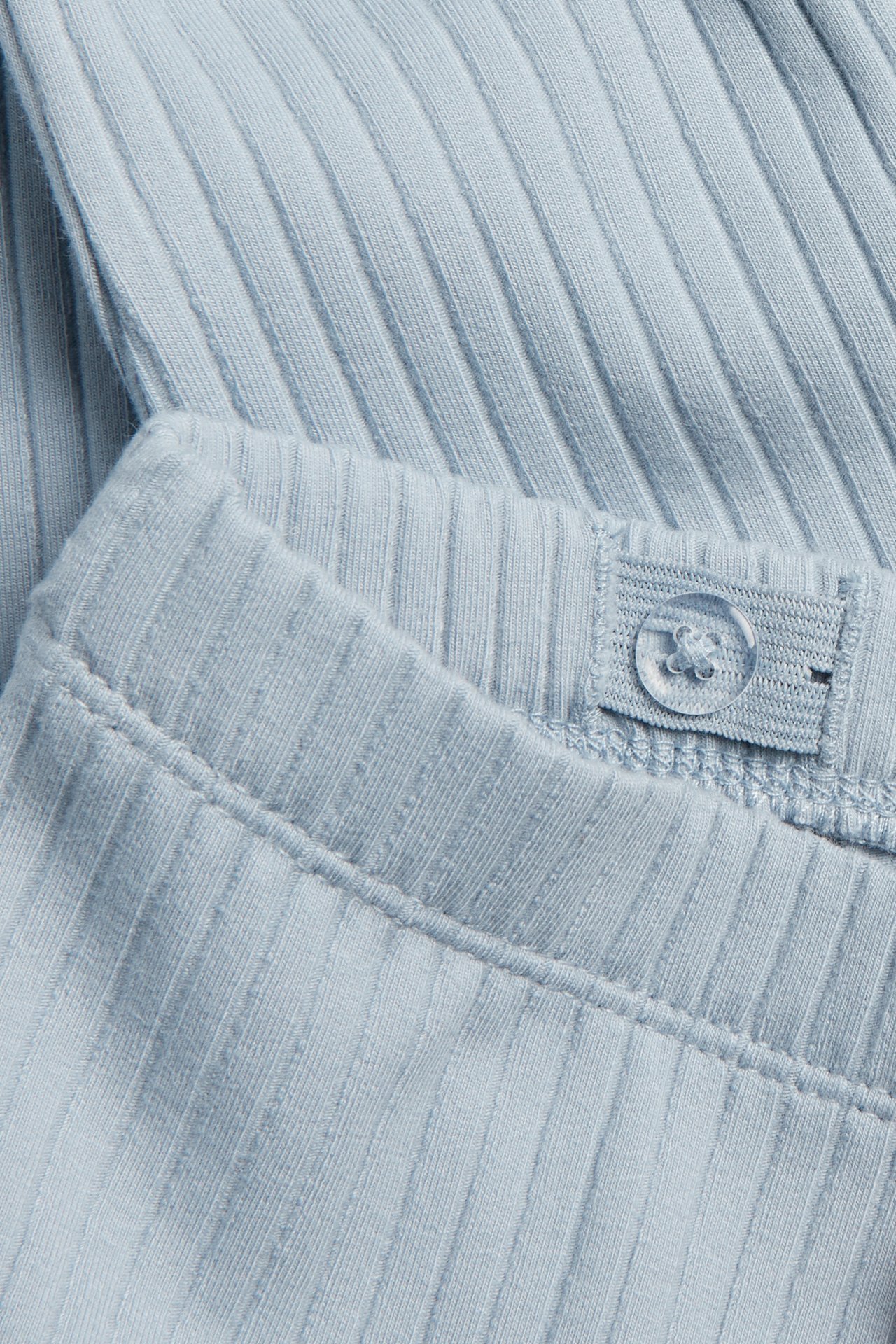 Nahaufnahme von hellblauen gerippten Leggings mit verstellbarem Gummibund und einem transparenten Knopf.