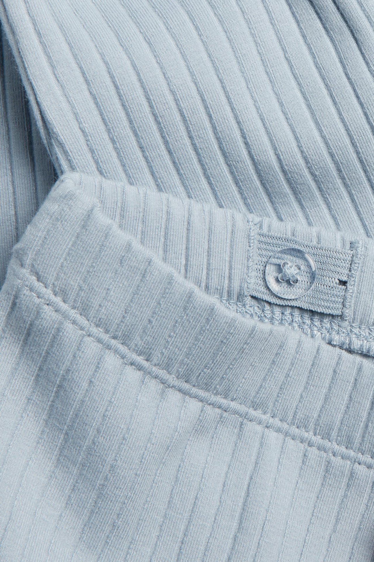 Nahaufnahme von hellblauen gerippten Leggings mit verstellbarem Gummibund und einem transparenten Knopf.