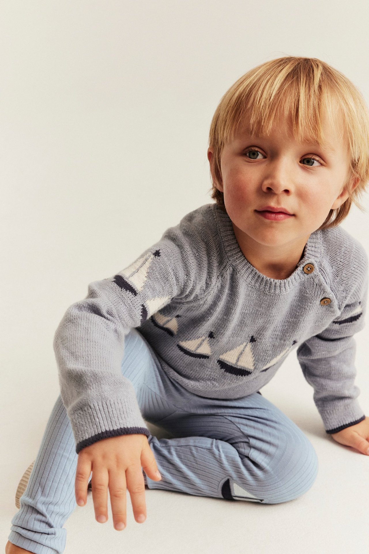 Vorderansicht eines Kindes in hellblauen gerippten Leggings mit Knieapplikationen und einem grauen Pullover mit Bootmuster.