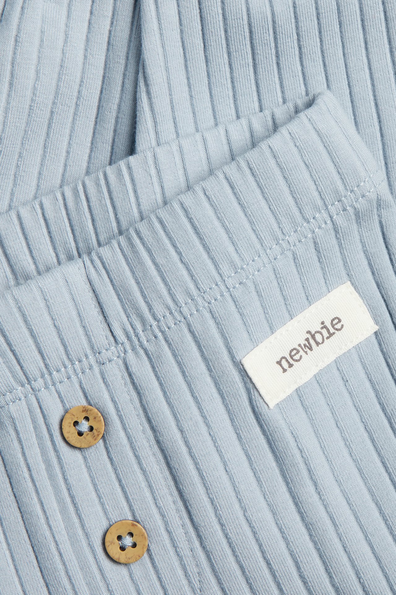 Close-up of light blue ribbed leggings with two wooden decorative buttons and a small white label.