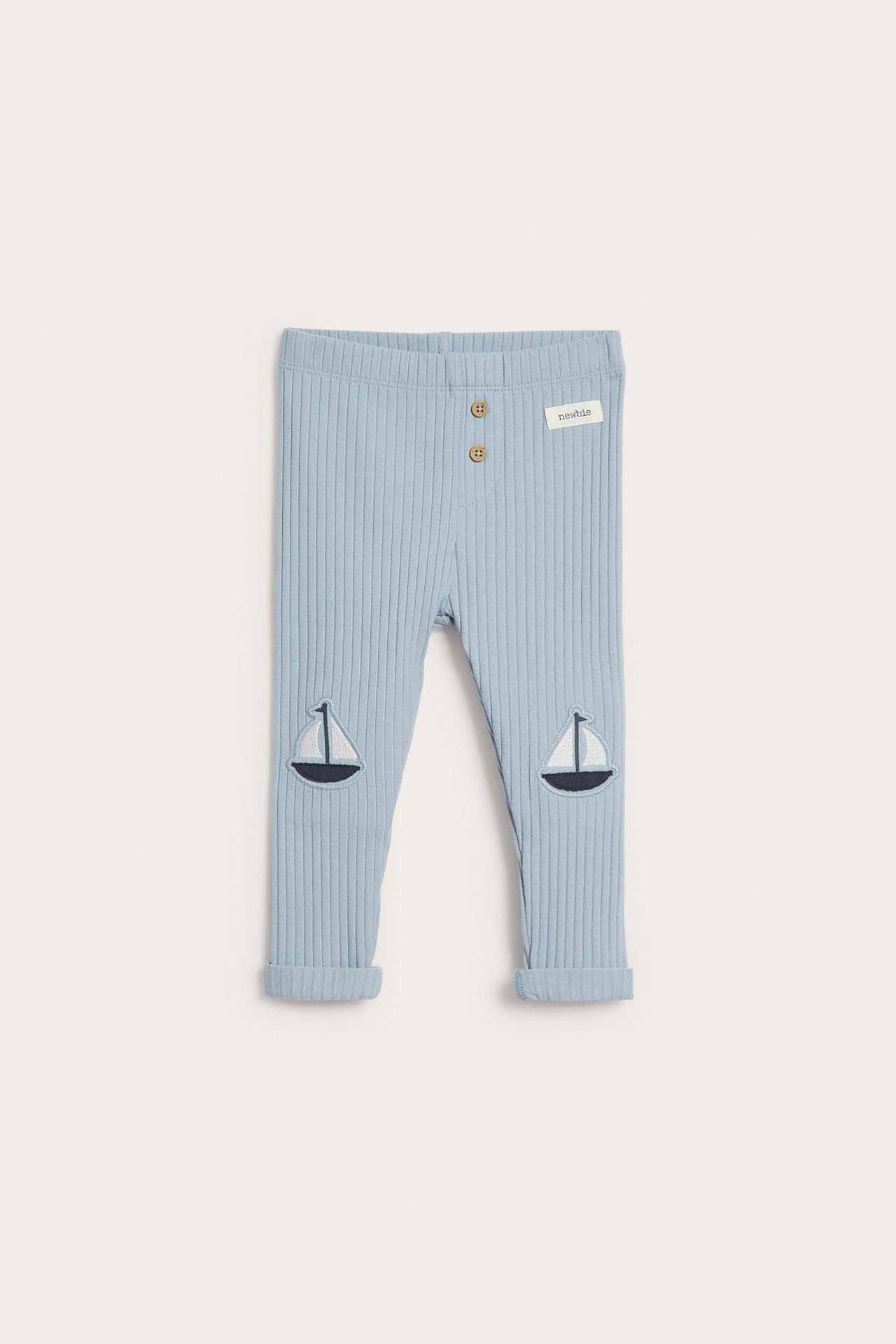 Vorderansicht babyhellblauer gerippter Leggings mit zwei Zierknöpfen und Segelboot-Knieapplikationen, umgekrempelten Bündchen.