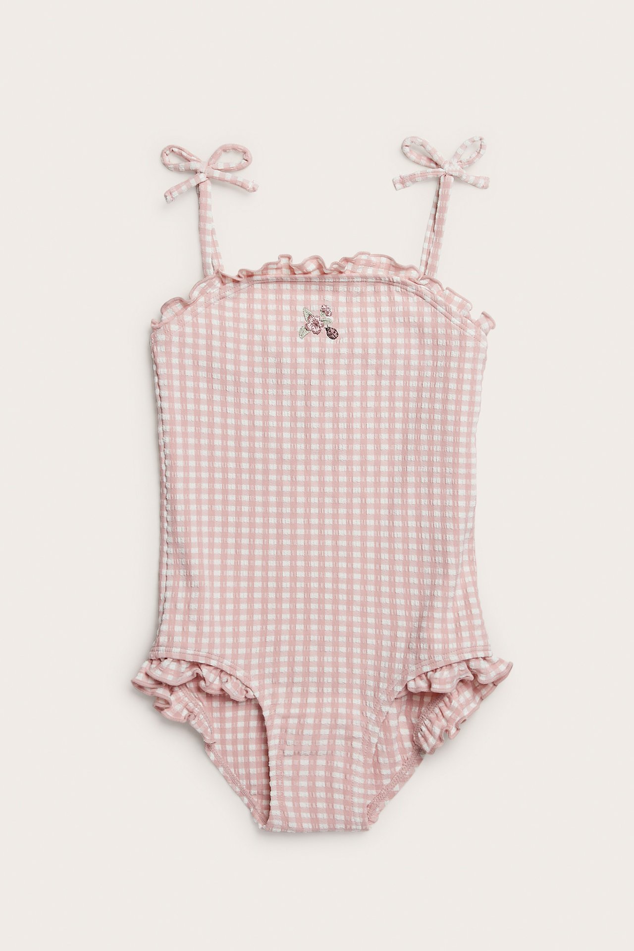 Front view of a kid's pink and white checked seersucker swimsuit with floral embroidery and bow shoulder straps.