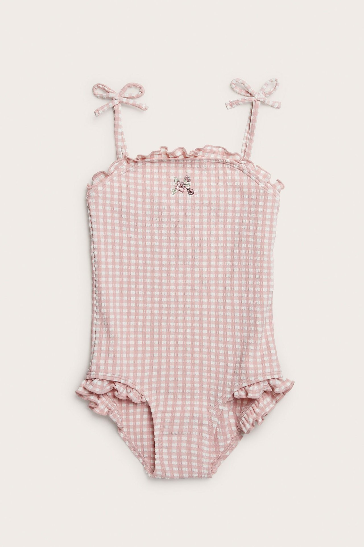 Front view of a kid's pink and white checked seersucker swimsuit with floral embroidery and bow shoulder straps.