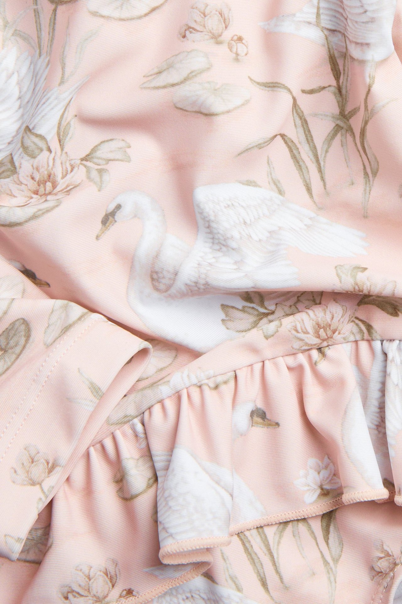 Nahaufnahme von rosafarbenem UV-Badeanzugstoff mit weißem Schwanen- und Blumenmuster, mit Rüschendetail.
