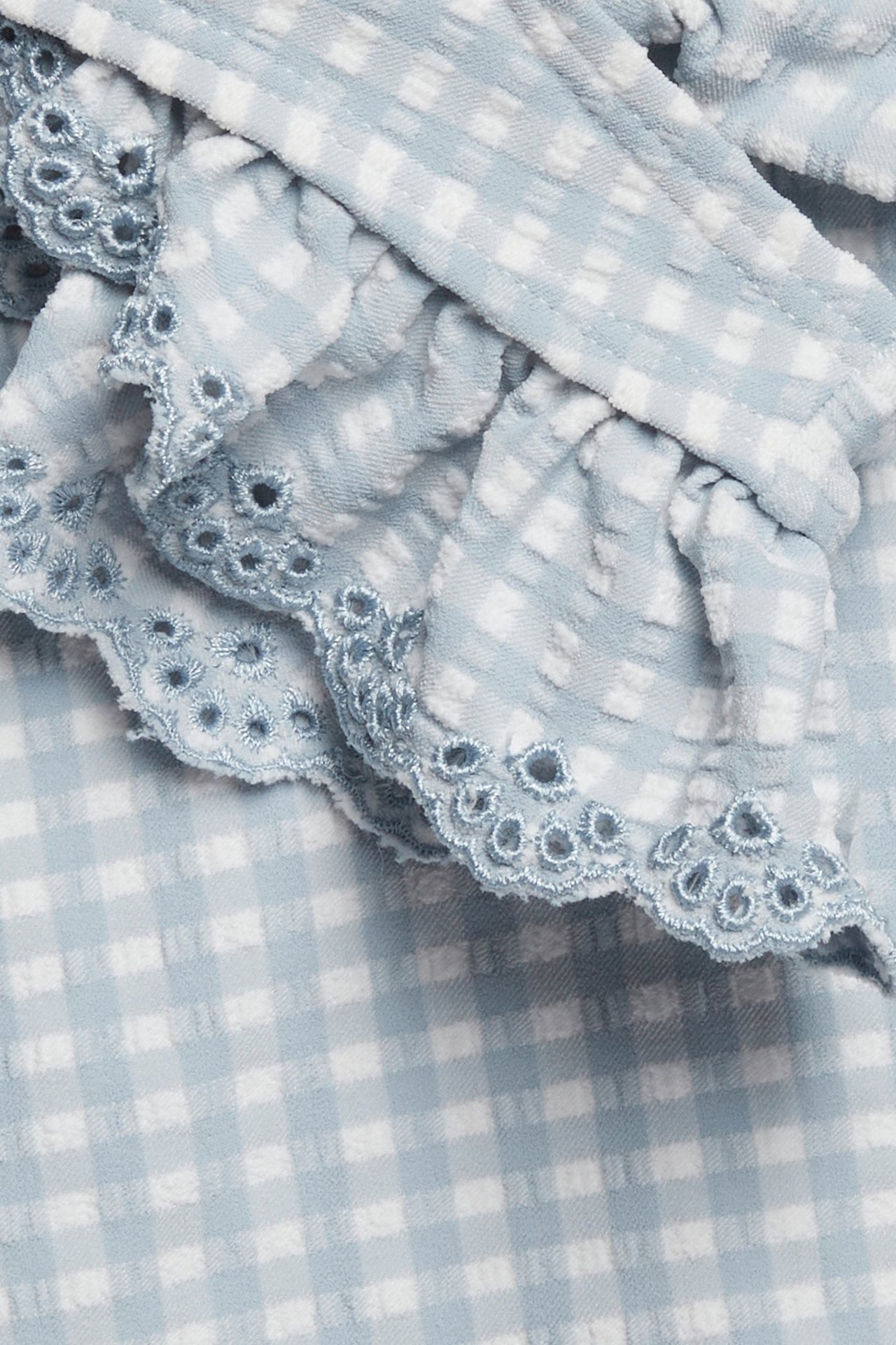 Close-up of a blue and white checkered seersucker swimsuit with ruffles and light blue eyelet embroidery.