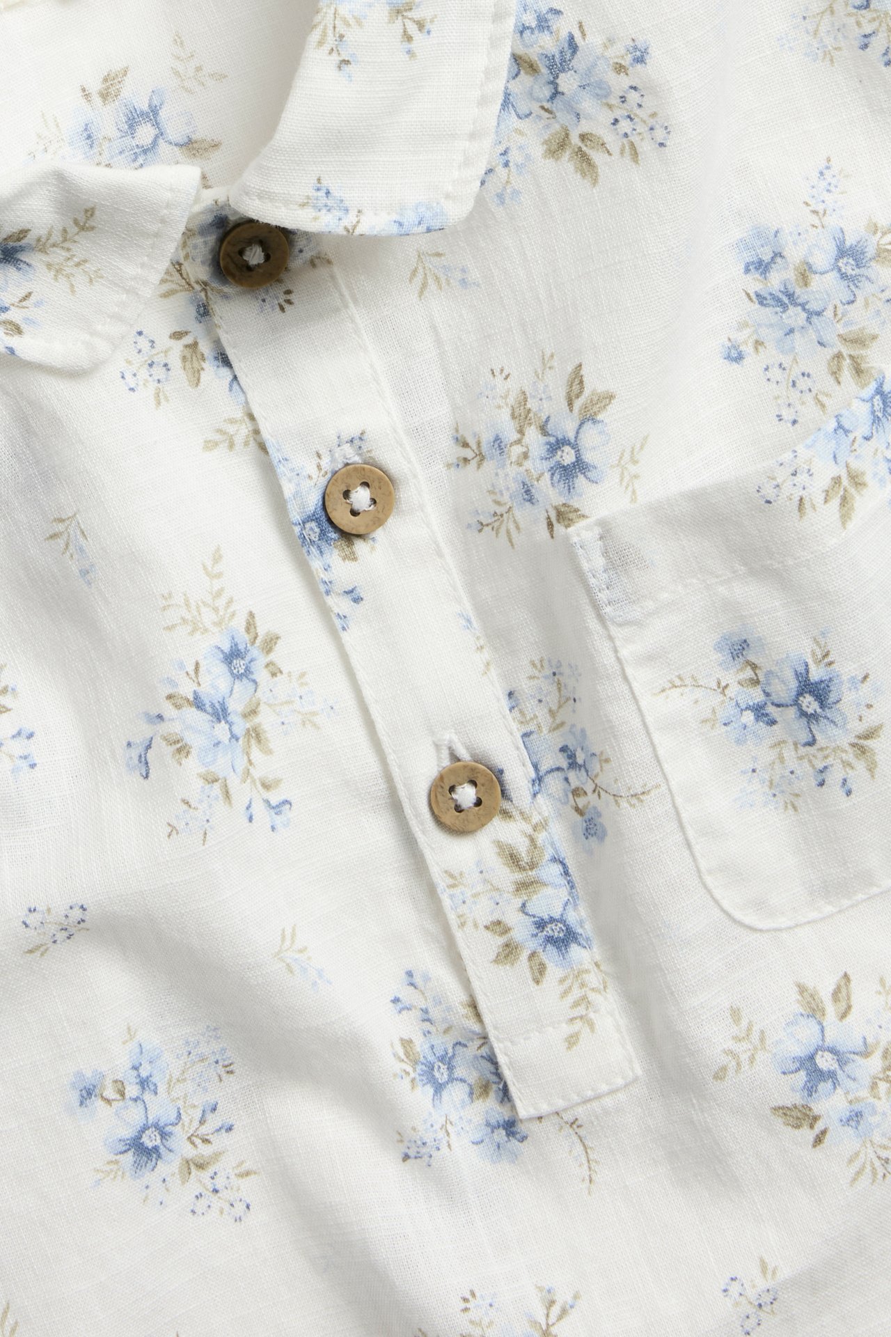 Close-up of an off-white cotton short-sleeved shirt with a blue floral pattern, collar, buttons, and chest pocket.