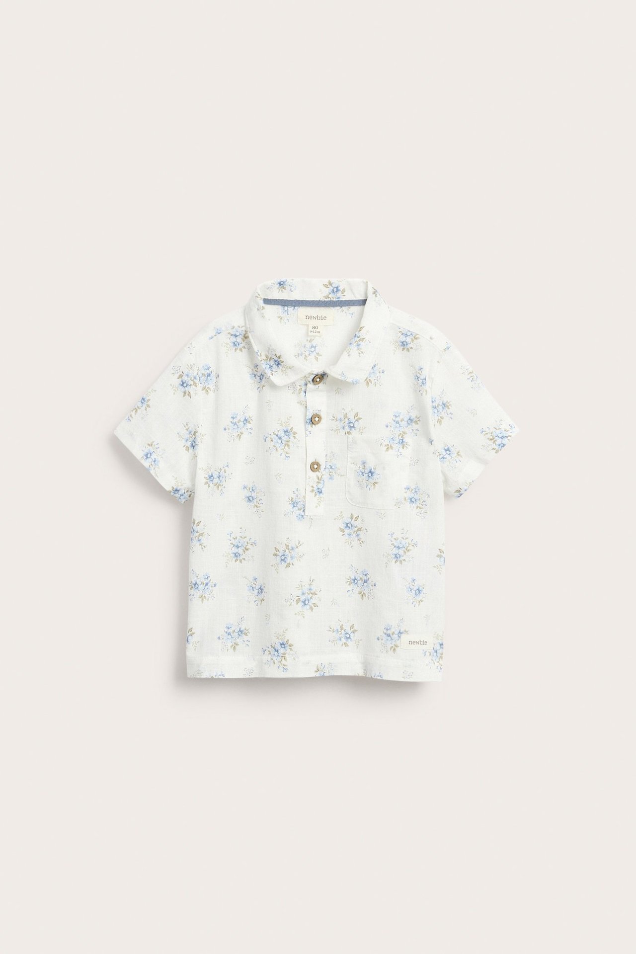 Front view: Off-white kid's short-sleeved shirt with blue floral pattern, collar, and button placket.