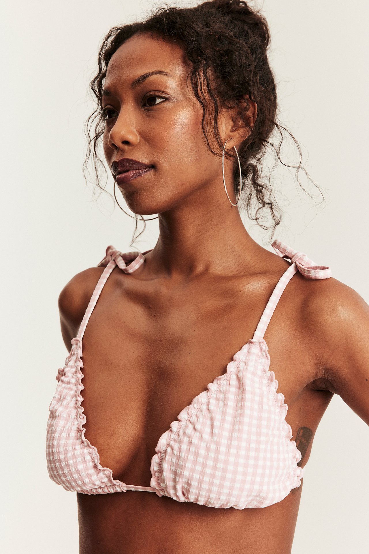 Front view: woman wears pink-white checkered triangle bikini top, tie shoulders, silver hoops.