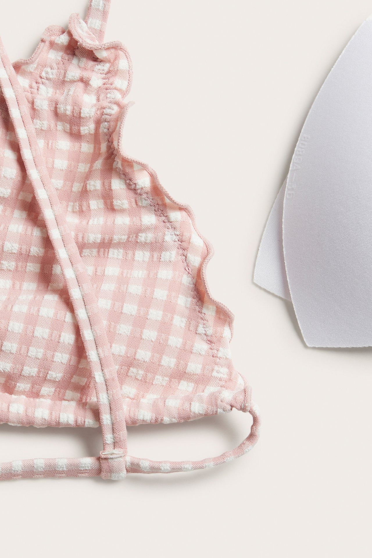 Close-up: Pink and white checkered triangle bikini top with ruffles, tie straps, and a white removable pad.