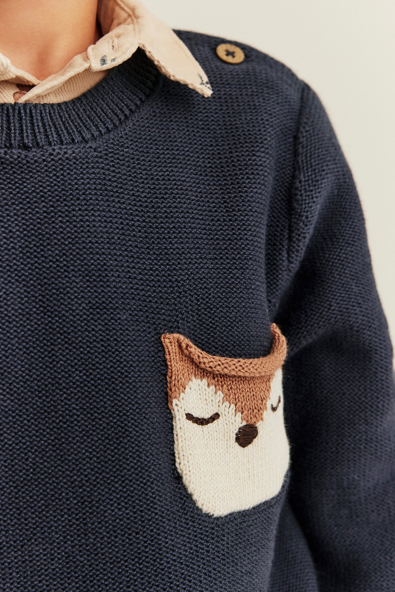 Close-up of a kid wearing a navy blue knitted sweater with a fox pocket.