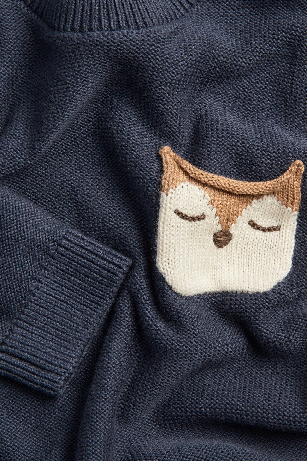 Nahaufnahme eines dunkelblauen Strickpullovers mit einem cremefarbenen und braunen Fuchsgesicht-Patch vorne.