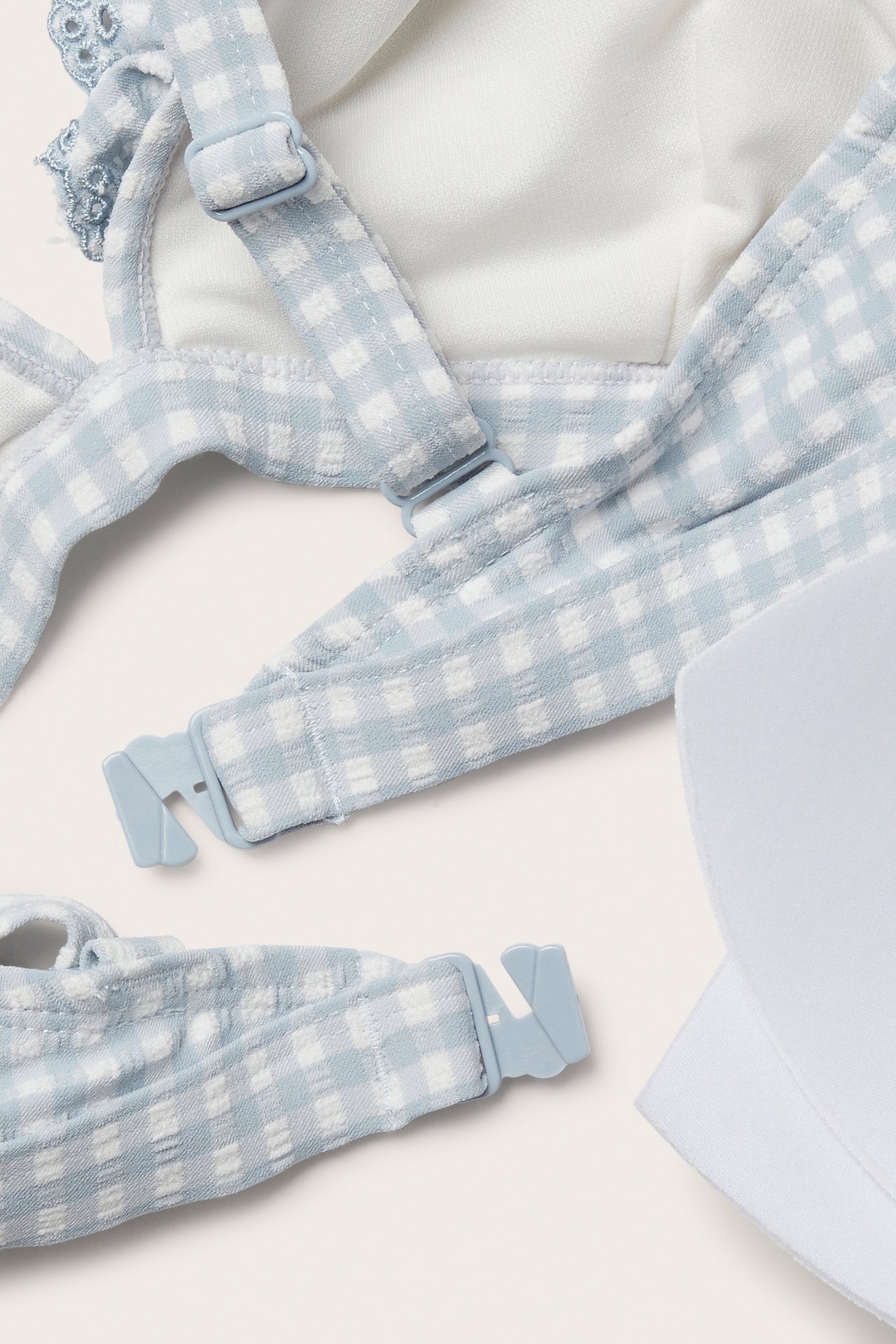 Nahaufnahme eines hellblauen karierten Bikini-Oberteils mit verstellbaren Trägern, Rückenverschluss und weißer herausnehmbarer Polsterung.