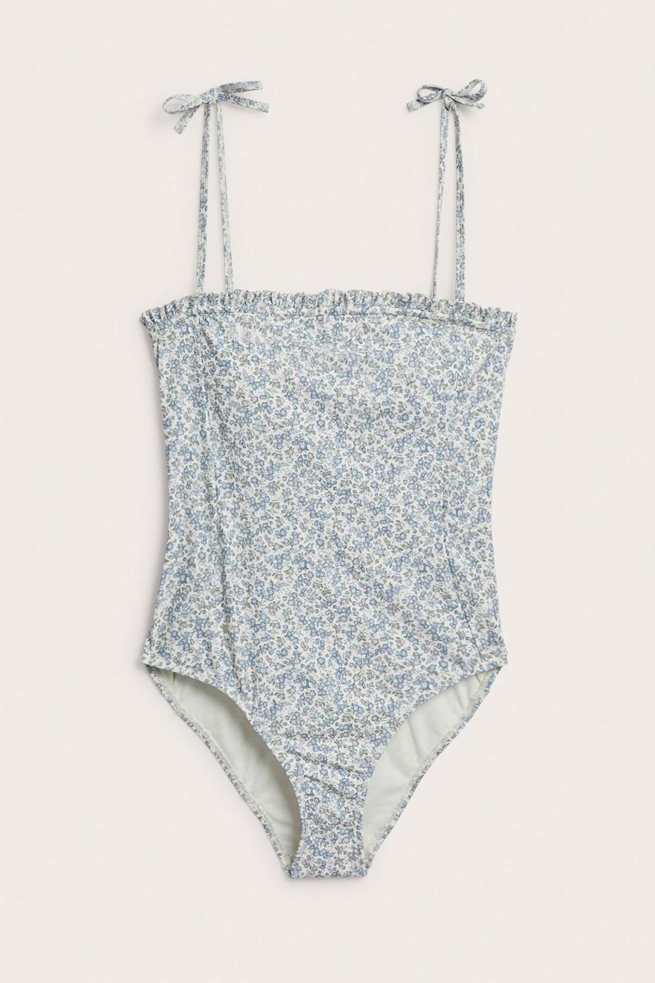 Vorderansicht eines grünen geblümten Badeanzugs mit Rüschenrand und Bindeträgern.