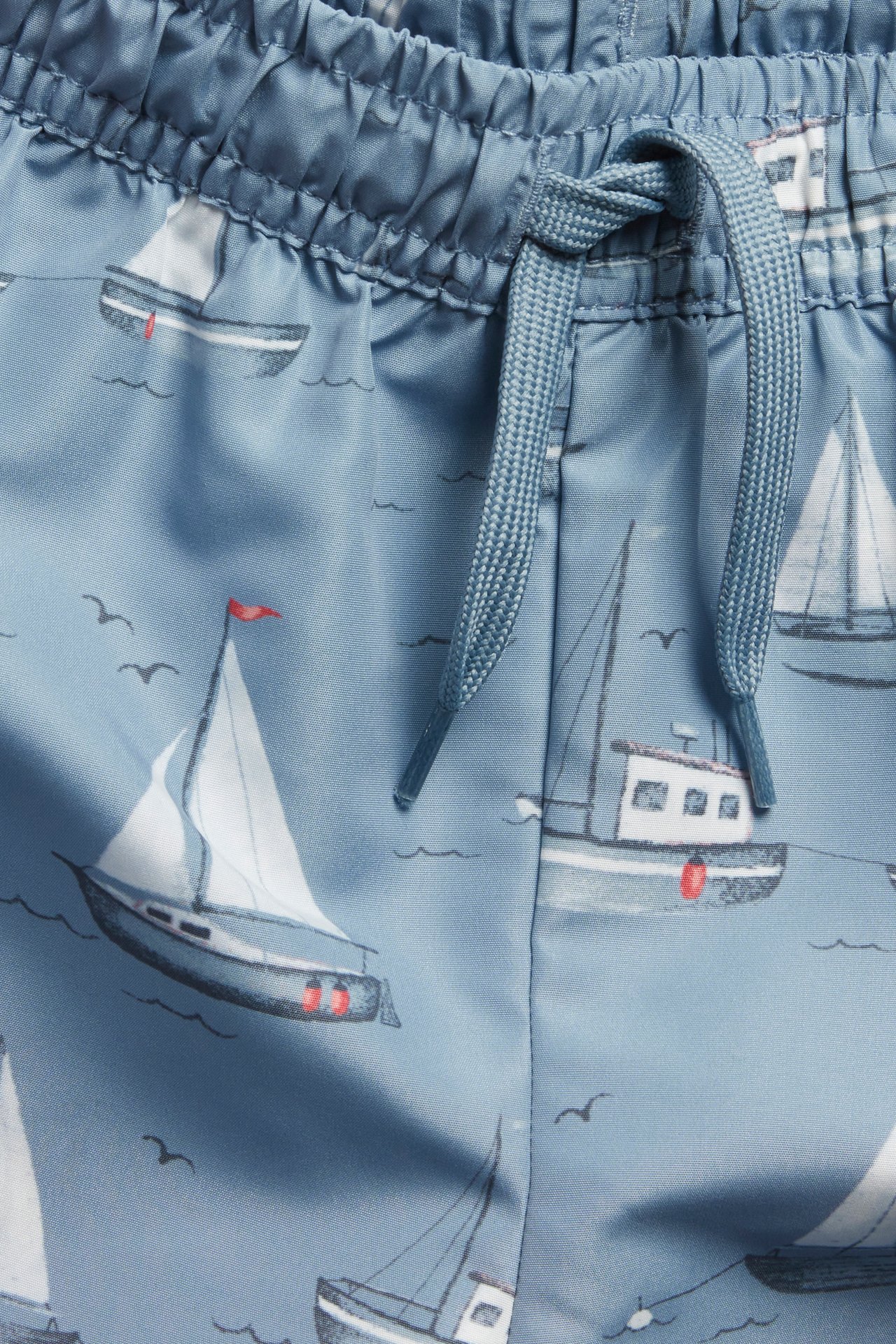Close-up of blue swim shorts with a white boat pattern and a blue drawstring.