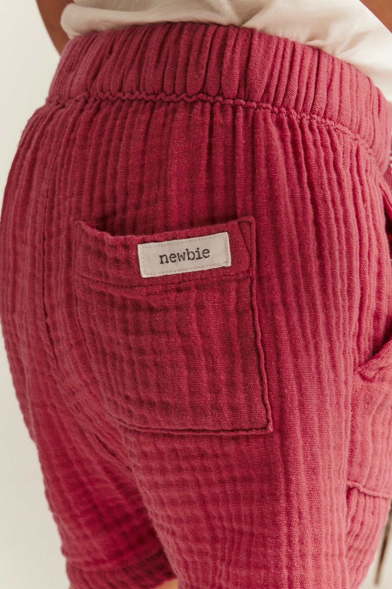 Nahaufnahme von hinten: Kind trägt rote gewebte Baumwollshorts mit Gummibund und aufgesetzter Gesäßtasche.