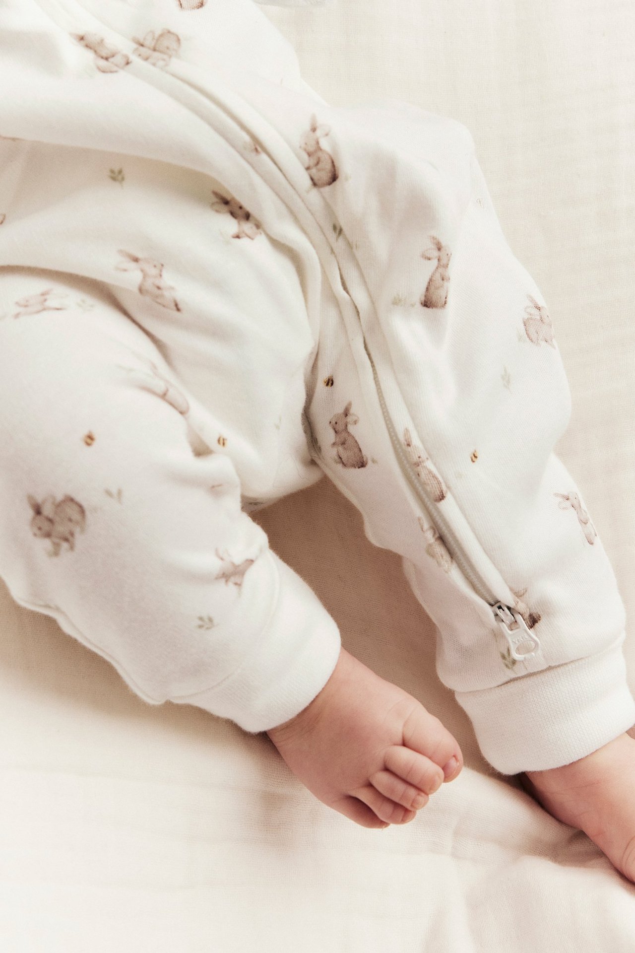 Nahaufnahme der Babybeine im off-white Baumwollpyjama mit Hasenmuster und Reißverschluss.