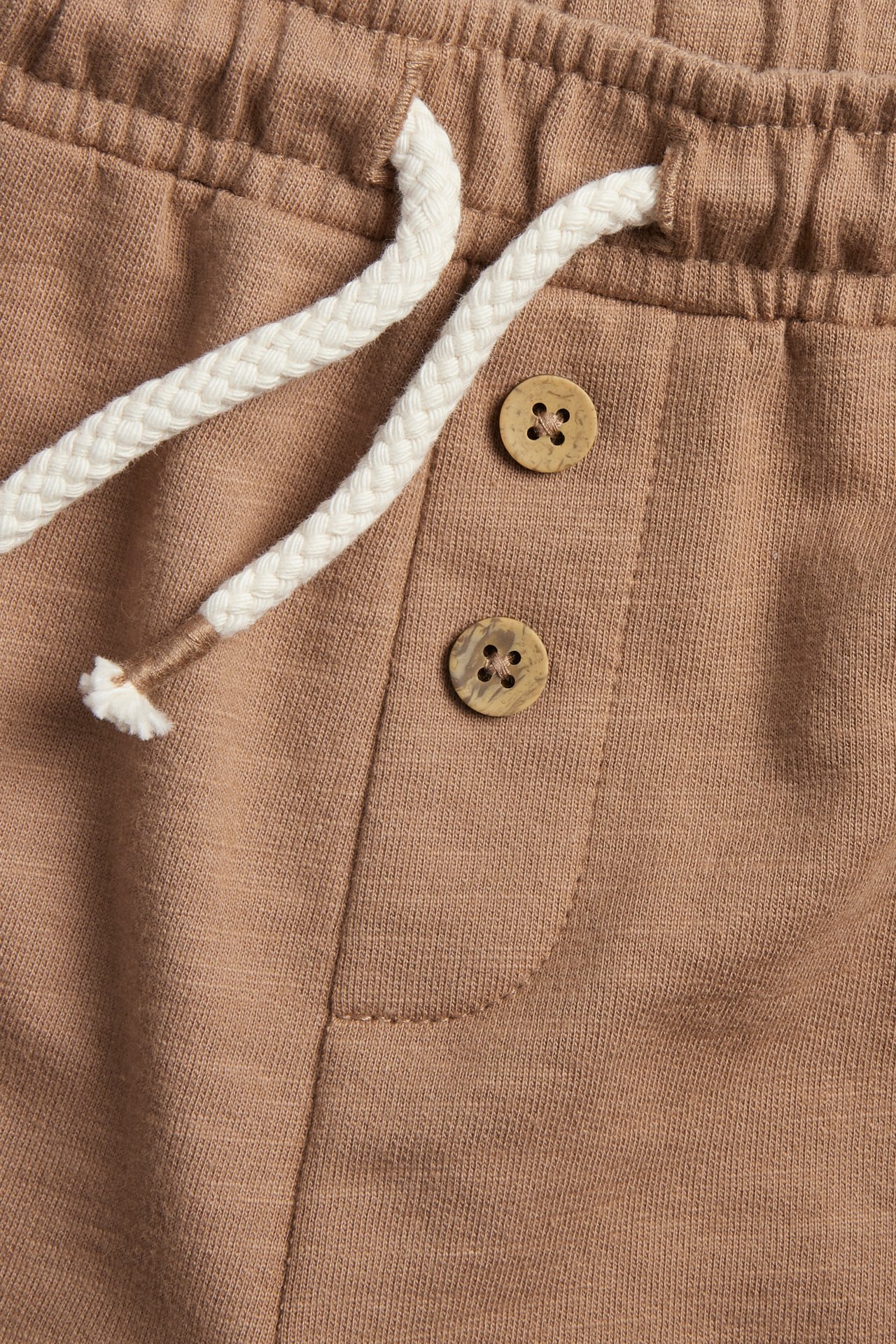 Close-up of brown slub jersey shorts with a white drawstring and two decorative wooden-look buttons.