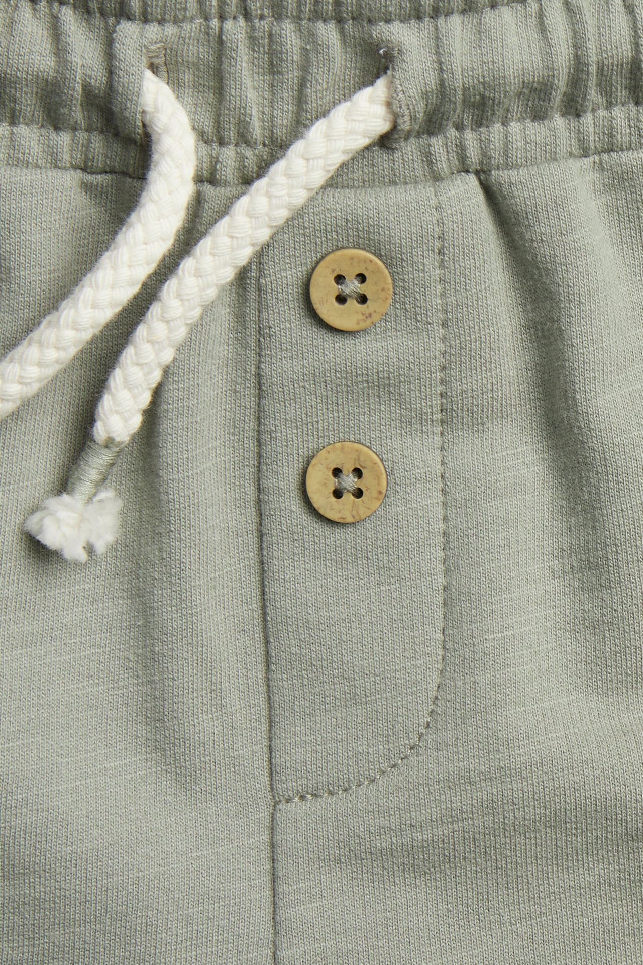 Nahaufnahme von dunkelgrünen Slub-Jersey-Shorts: elastischer Bund, weißer Kordelzug, dekorative braune Knöpfe.
