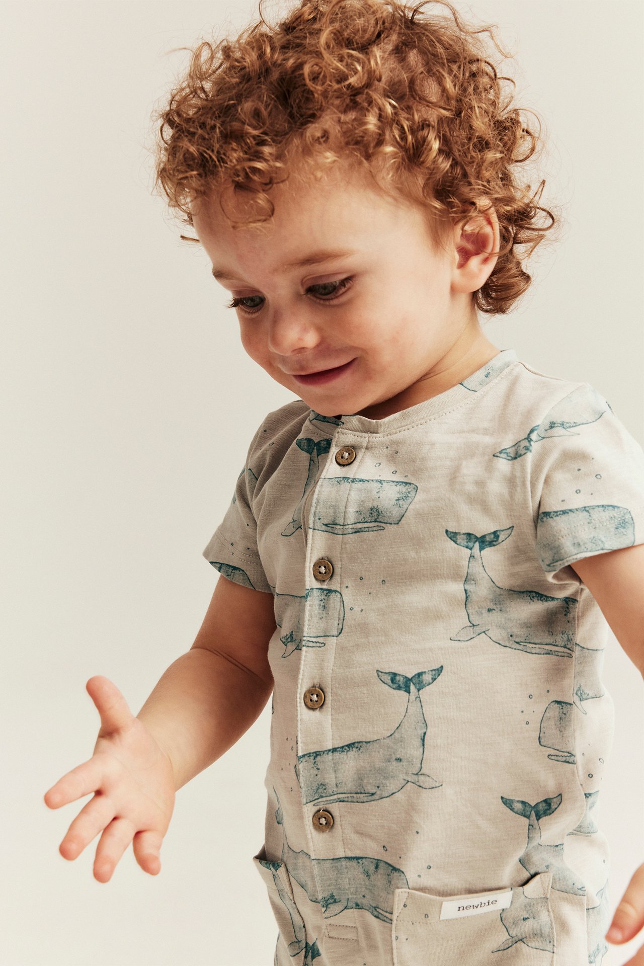 Front view of a baby wearing a short-sleeved beige cotton romper with a blue whale pattern and front buttons.