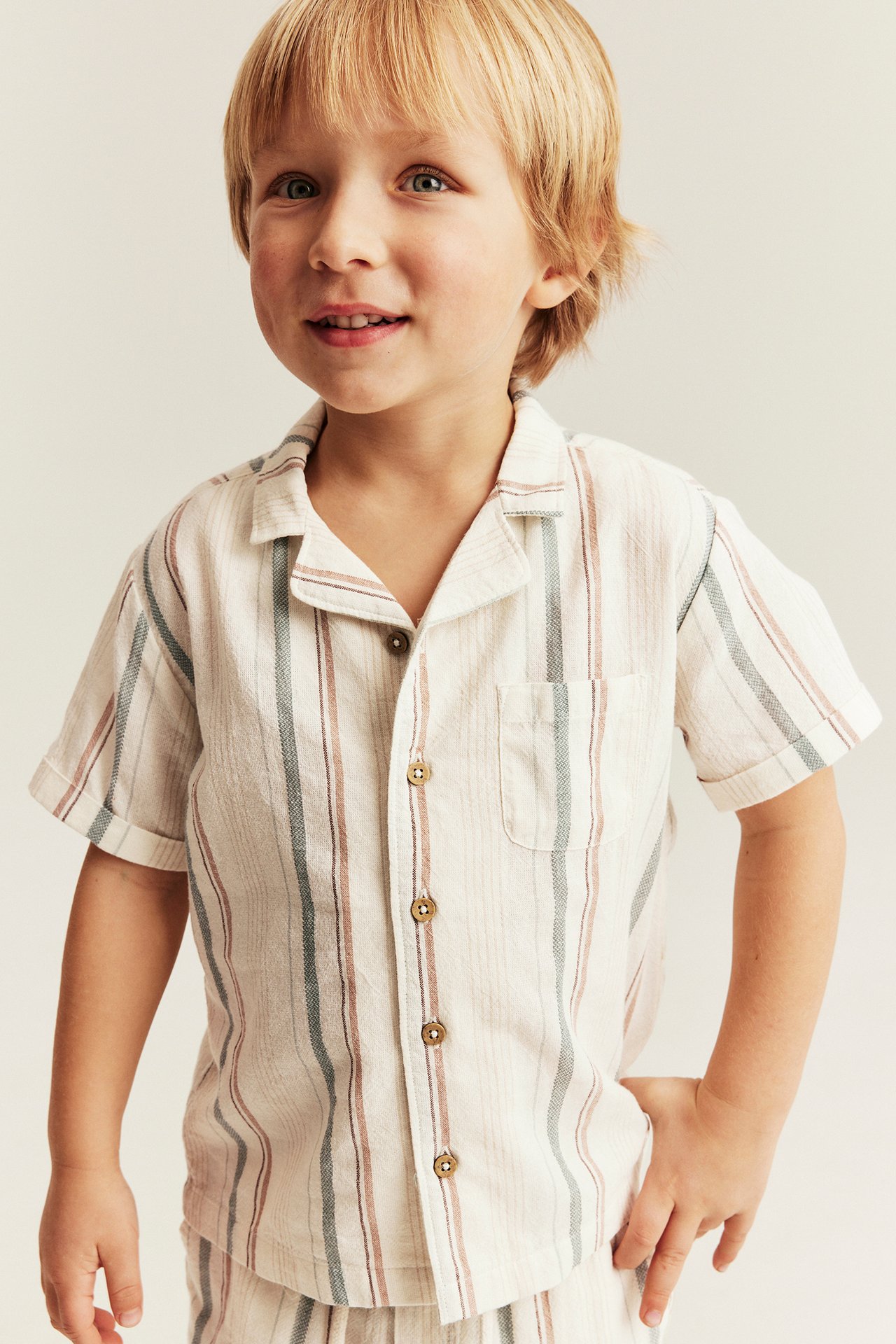 Front view of a kid wearing an off-white striped short-sleeved cotton shirt and matching shorts.