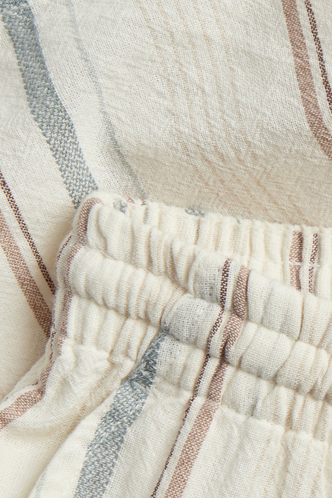 Nahaufnahme von off-white gestreiften gewebten Baumwollshorts mit elastischem Bund und braunen sowie blauen Streifen.