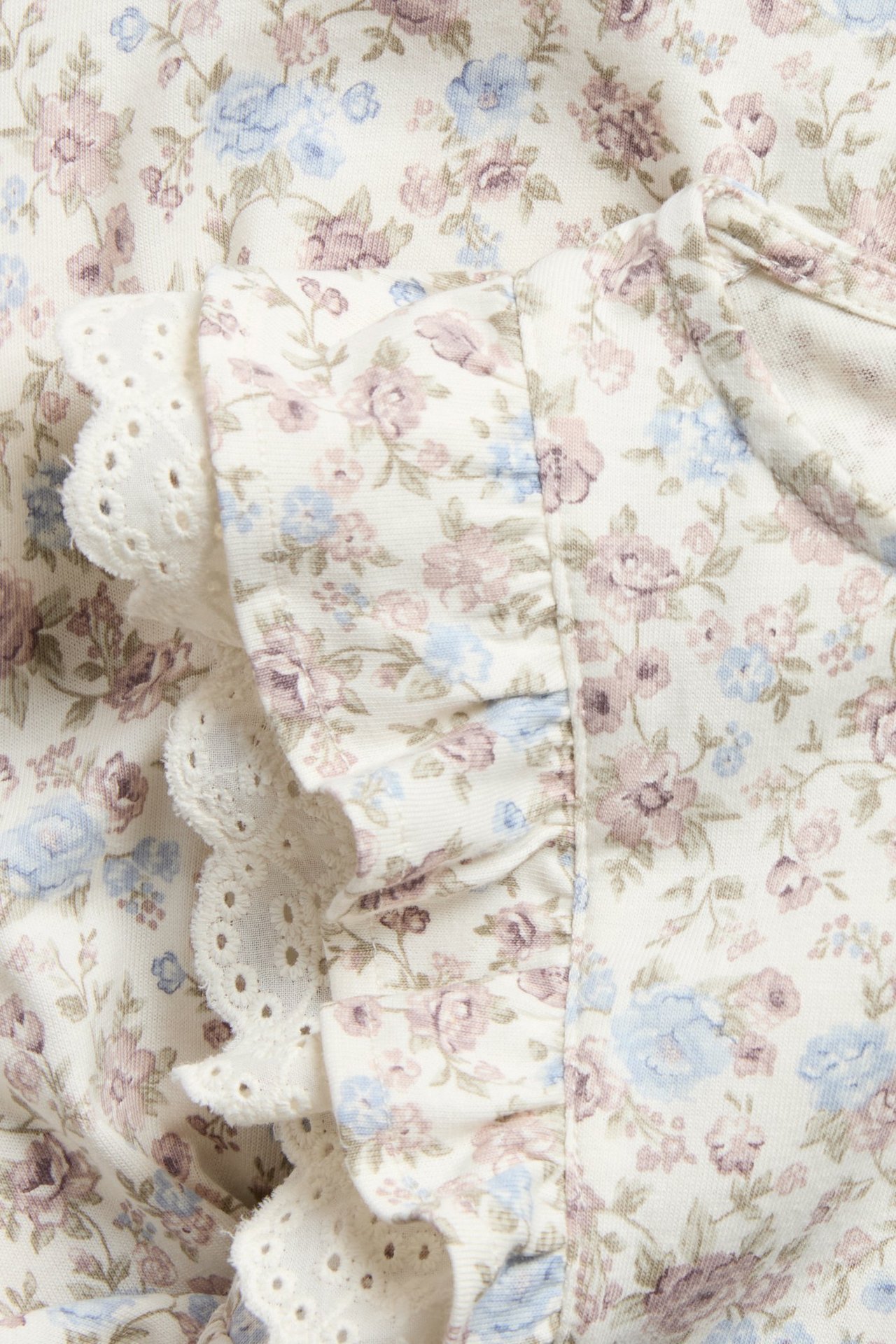 Close-up of an off-white cotton dress with small floral pattern, fabric ruffles, and white eyelet lace.