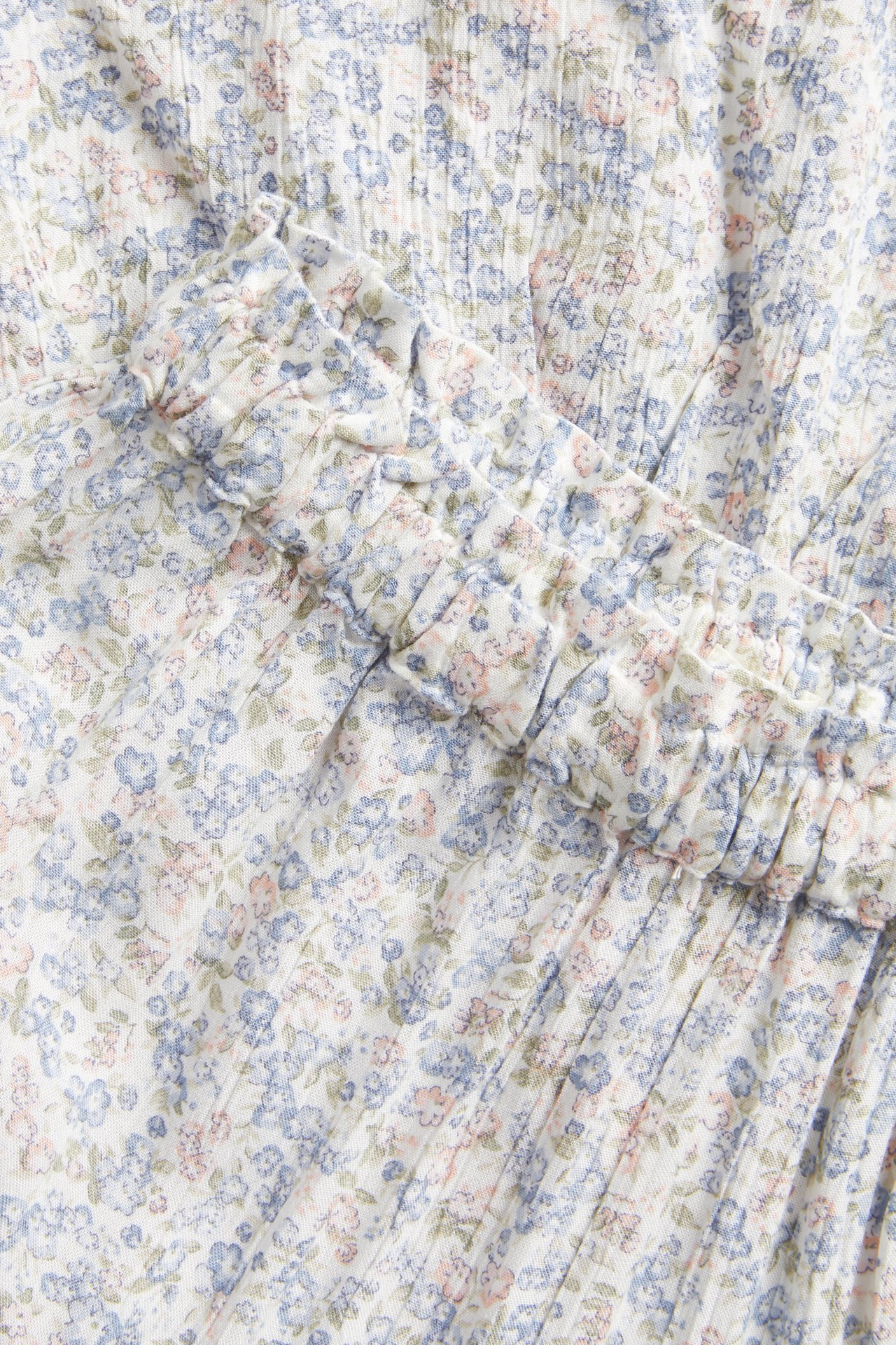 Nahaufnahme eines cremeweißen floralen langen Rocks mit kleinen blauen und rosa Blüten und Rüschendetail.