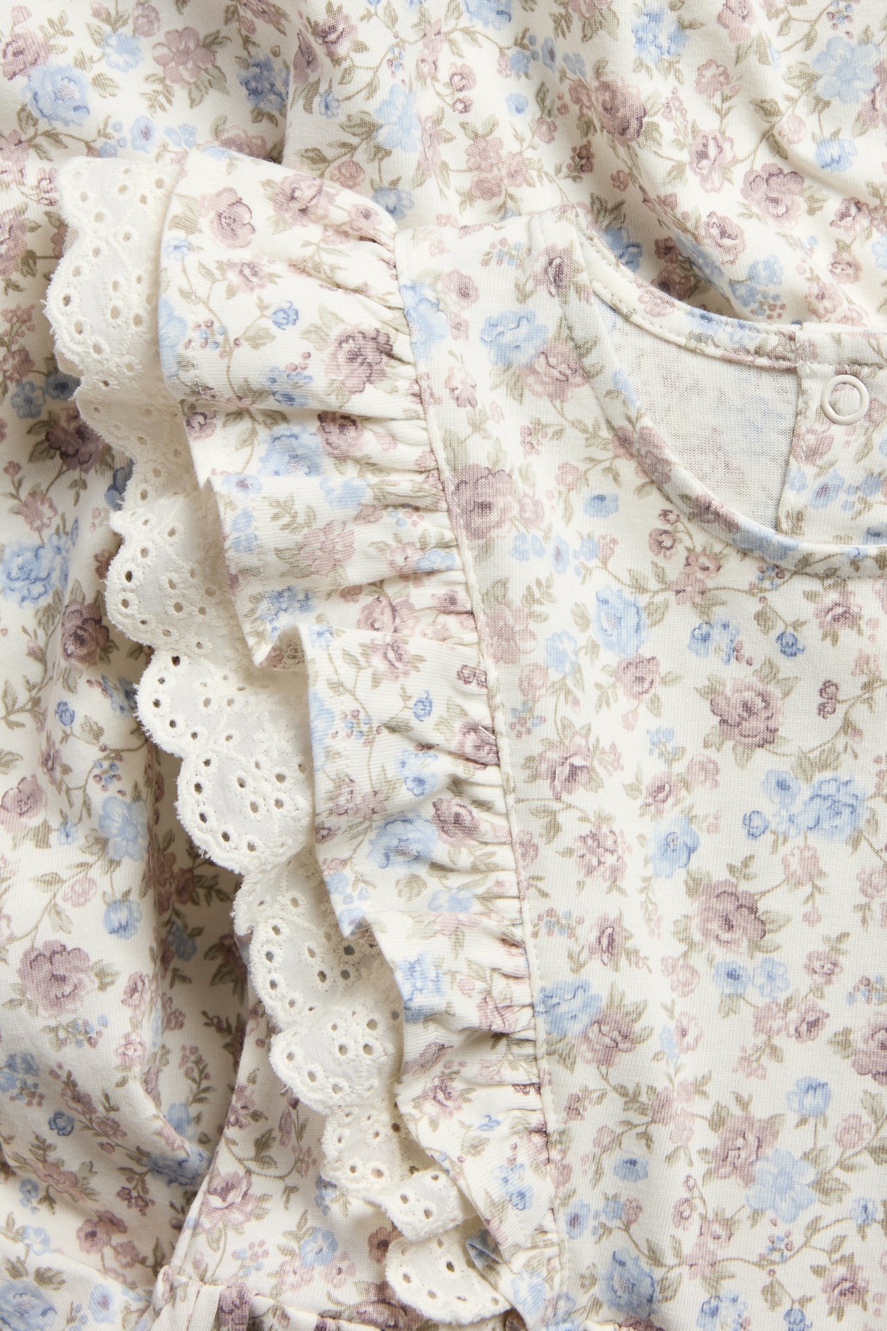 Nahaufnahme: Off-weißes florales Baumwoll-Jerseystrickkleid mit Rüschen und weißer Lochstickerei-Spitze.