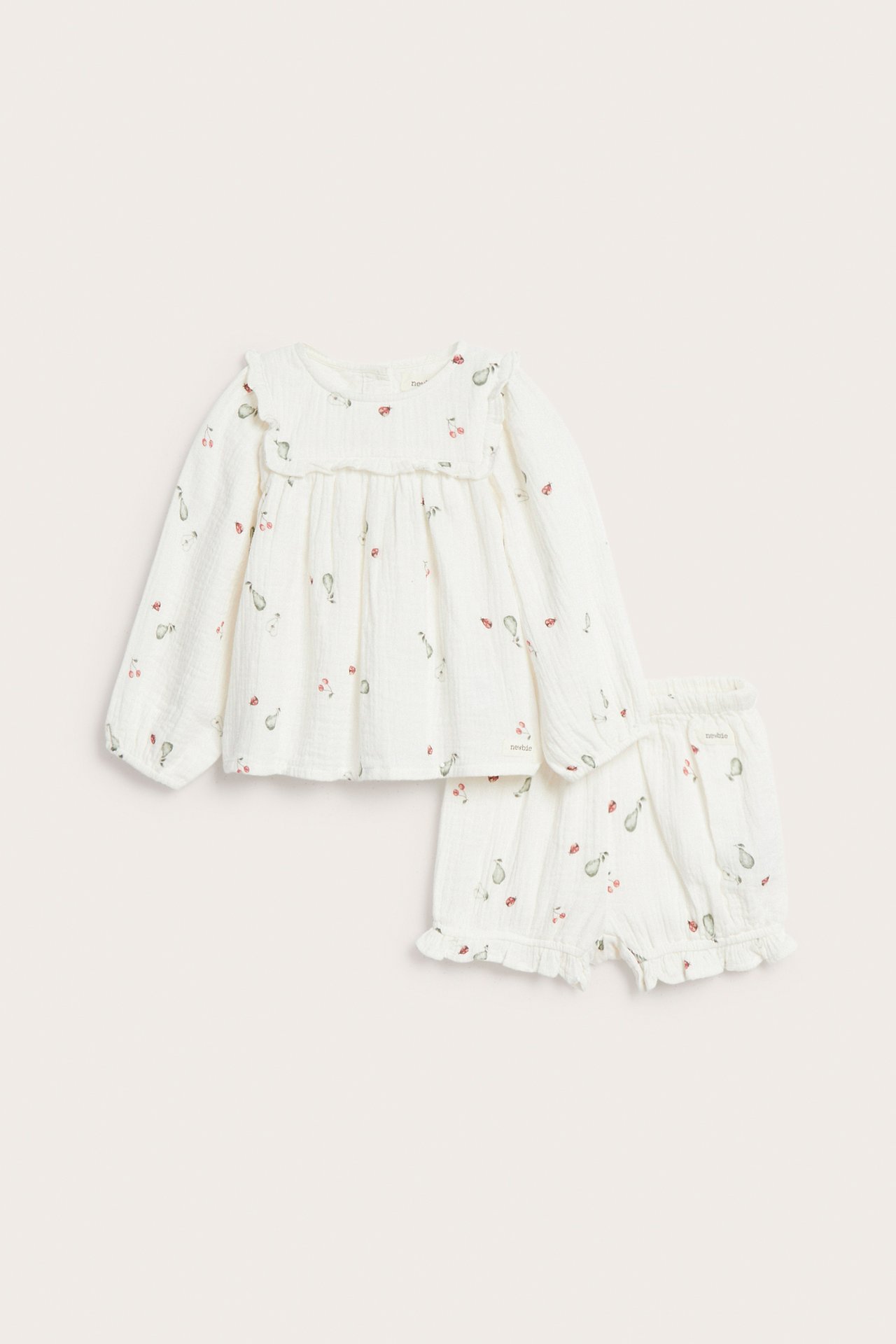 Front view of an off-white muslin baby set with long-sleeved blouse with ruffle yoke and patterned shorts.