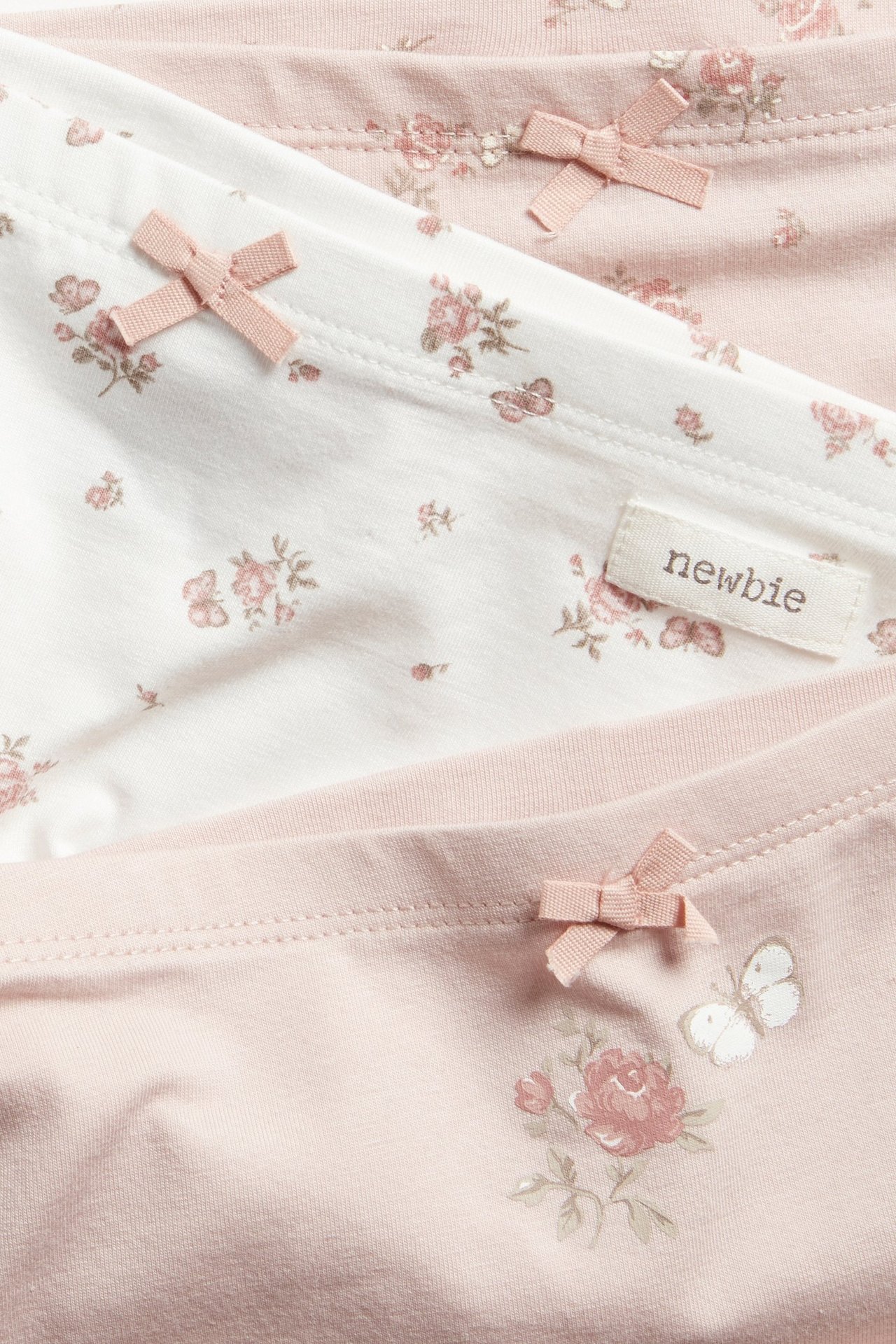Nahaufnahme von drei Kinder-Boxershorts: eine weiße, zwei rosafarbene, alle mit Blumenmuster und kleinen rosa Schleifen.